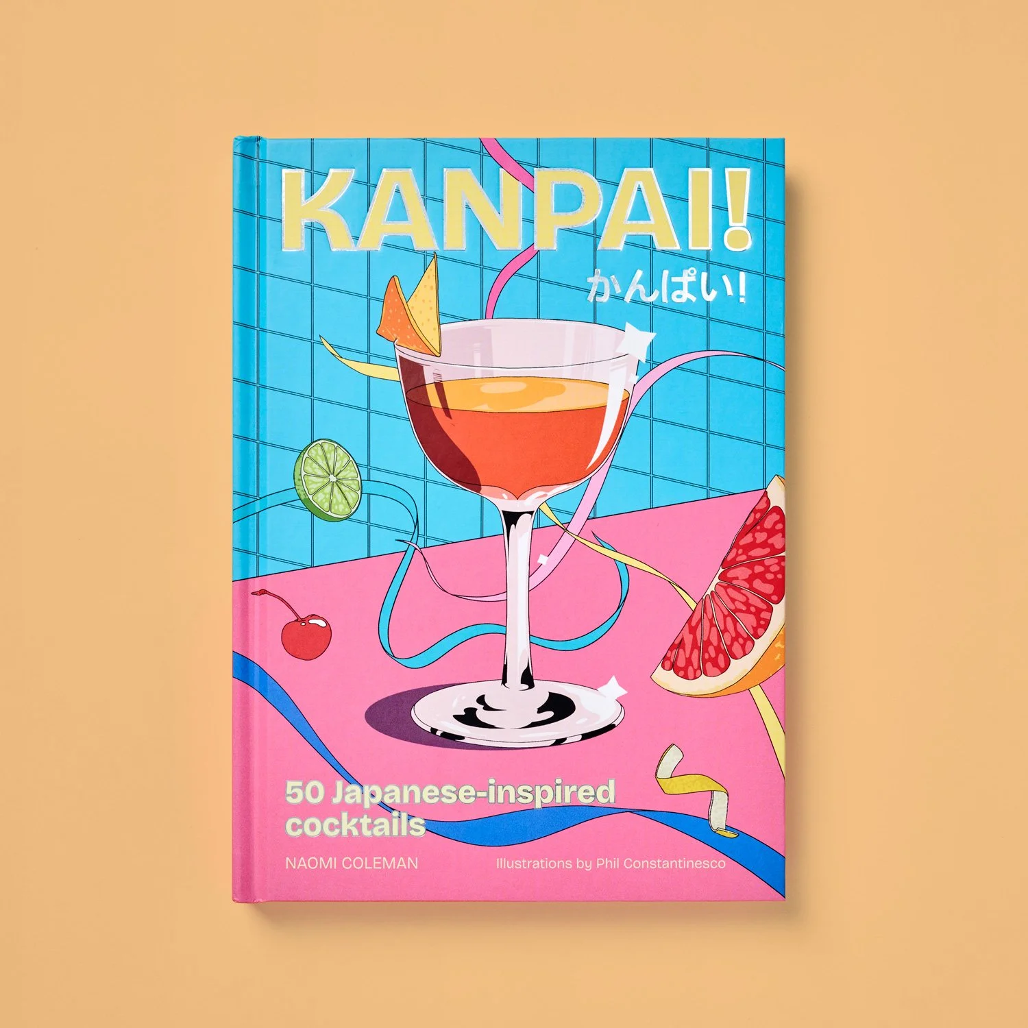 Book titled 'Kampai!' with an illustration of a cocktail glass filled with an orange-red drink, decorated with a slice of orange and a lime wedge, set against a vibrant, colorful background with fruits and streamers.