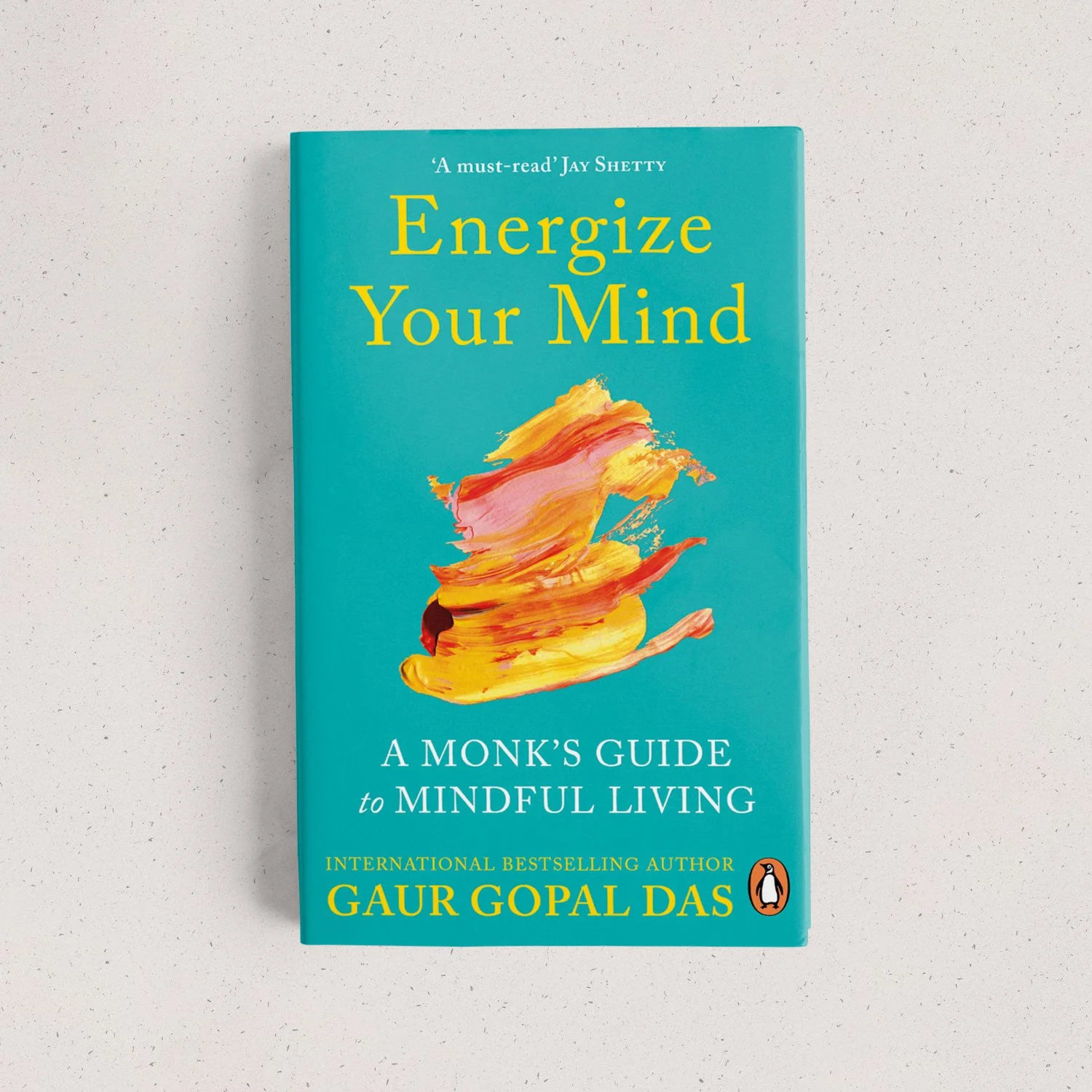 A book titled 'Energize Your Mind' by Gaur Gopal Das, with a blue cover and an abstract colorful illustration, placed on a light textured surface.