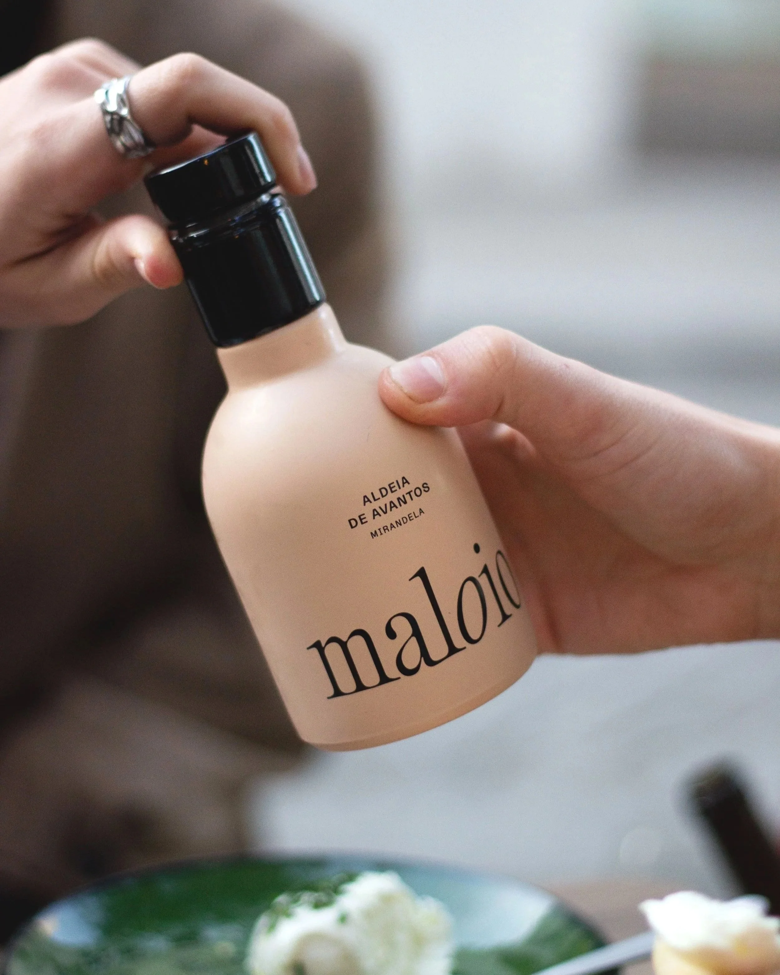 Pessoa segurando uma garrafa de vidro com rótulo que diz 'Aldeia de Avantos Mirandela' e 'maloio'