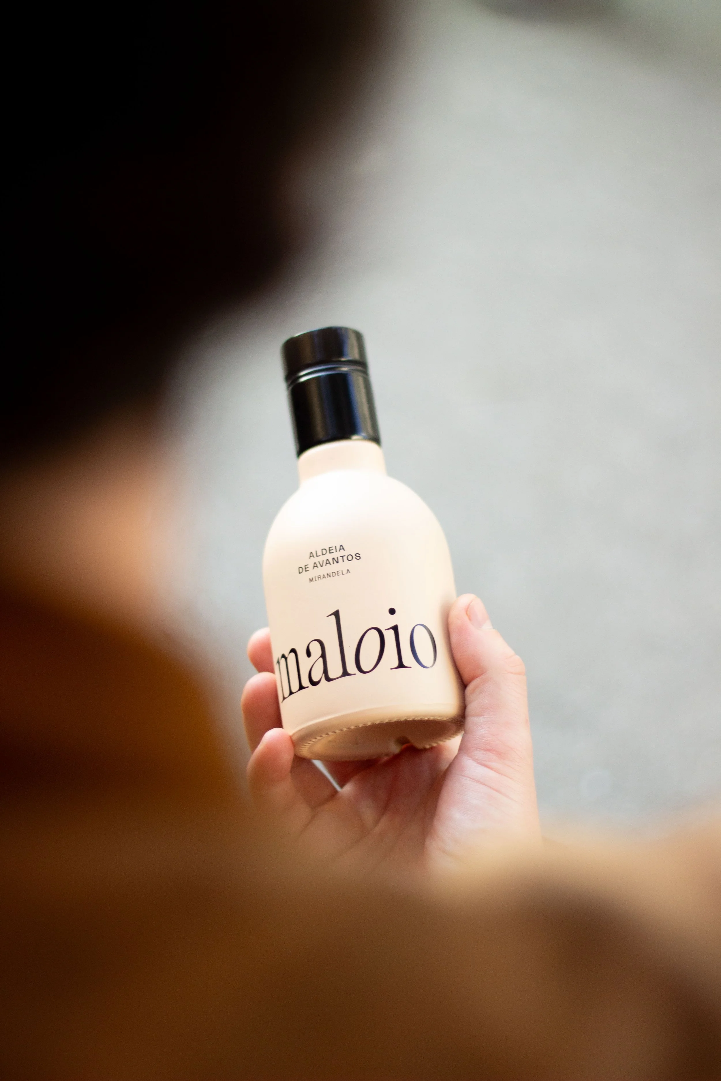 Pessoa segurando uma garrafa de creme ou loção com rótulo em português que diz "maloiô" e "aldeia de avantos mirandela".