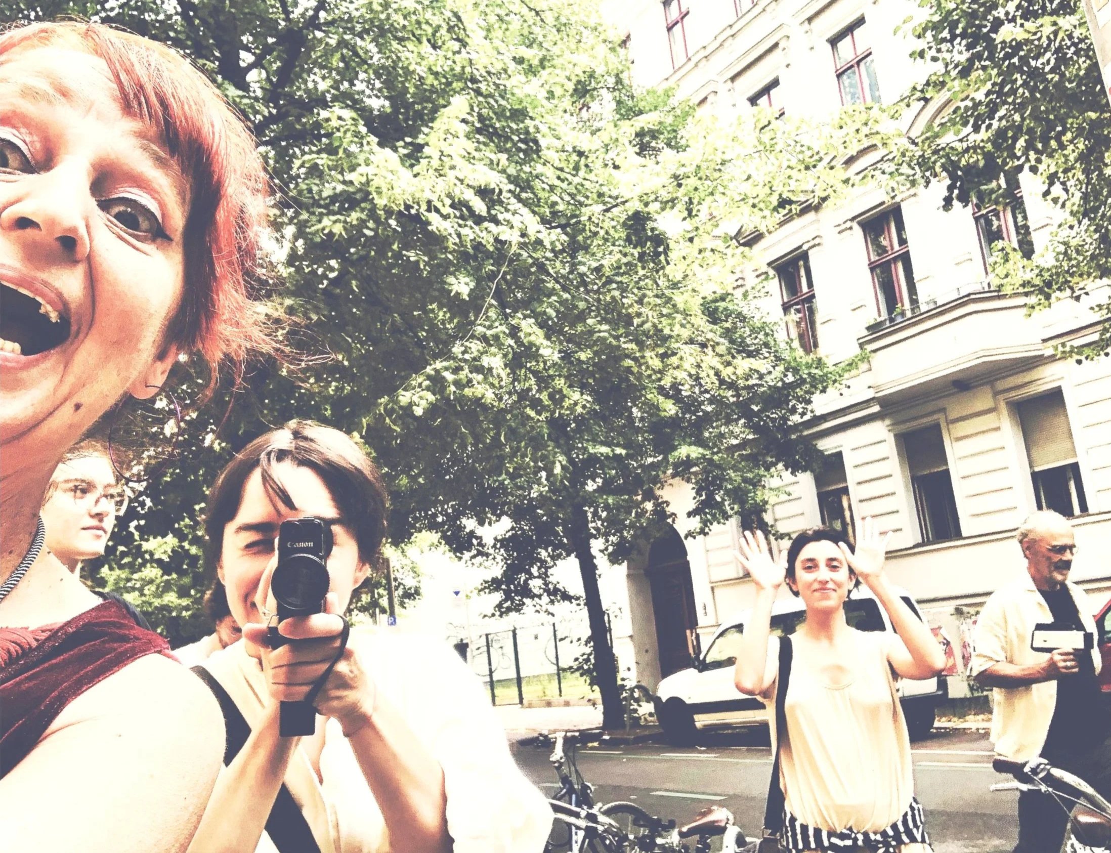 Mehrere Menschen fotografieren und posieren auf einer Straße vor einem großen Baum und einem alten Gebäude.