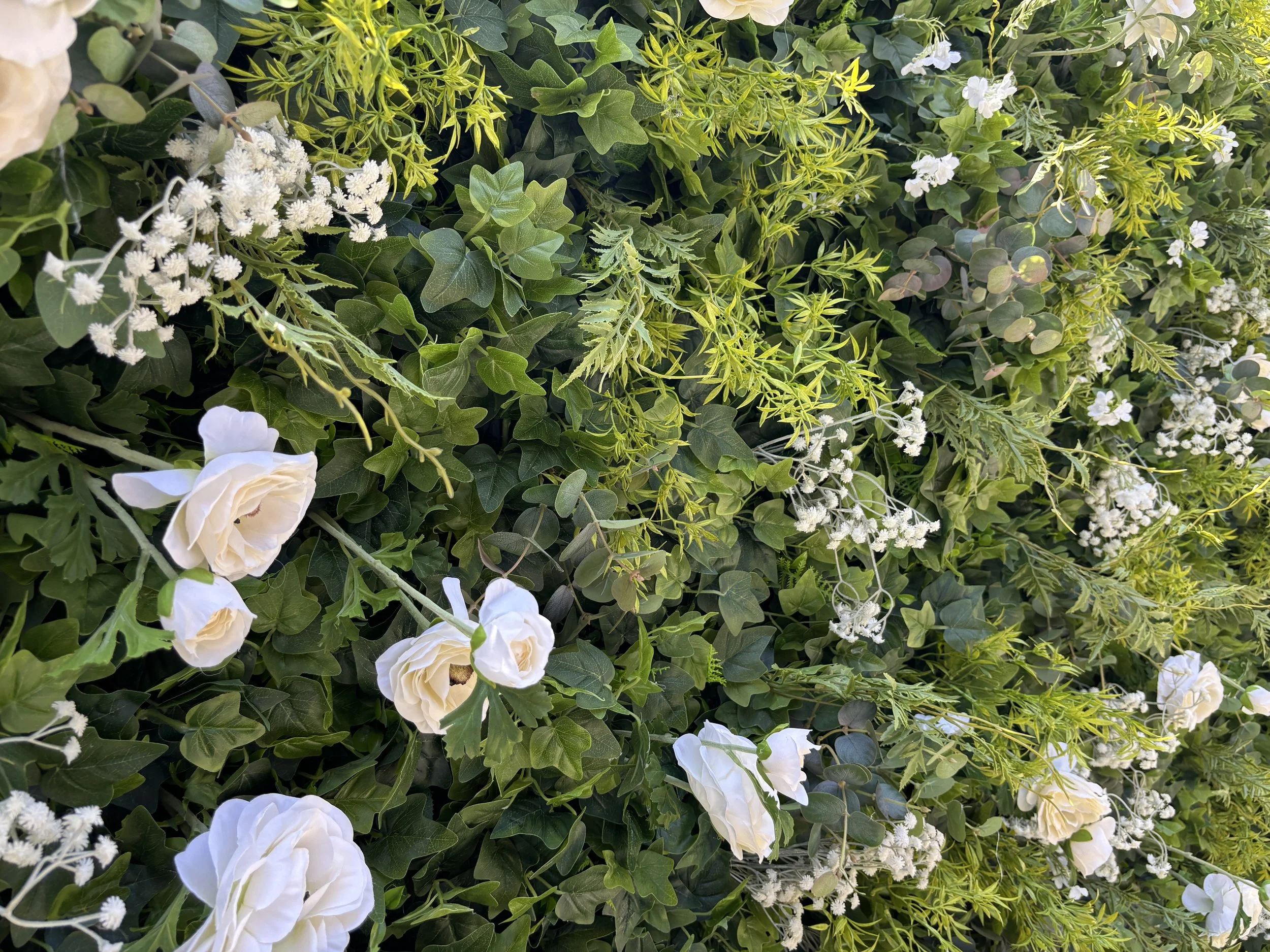 Close-up of The Lola flower wall featuring lush greenery, white roses, and delicate white florals.