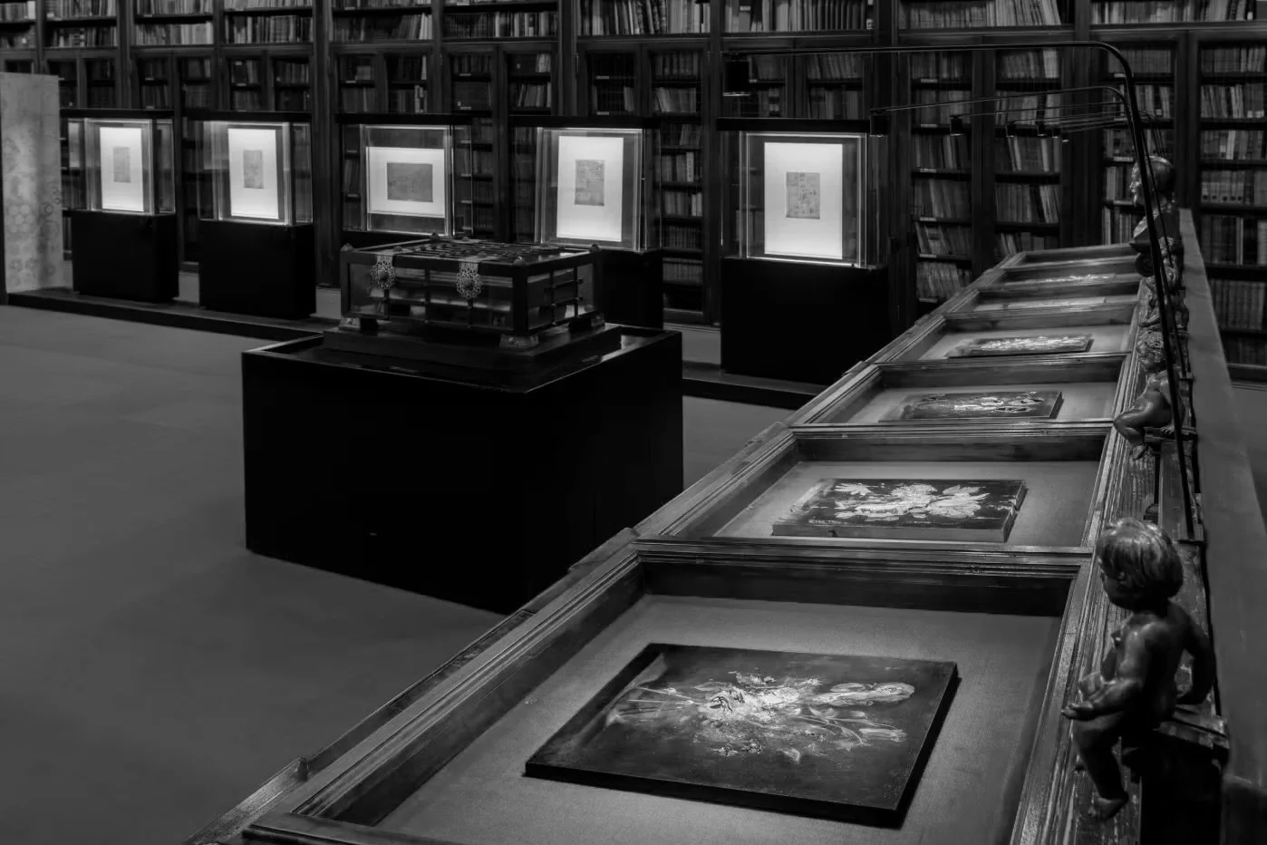 Sala di una biblioteca con opere d'arte e libri in esposizione, in bianco e nero.