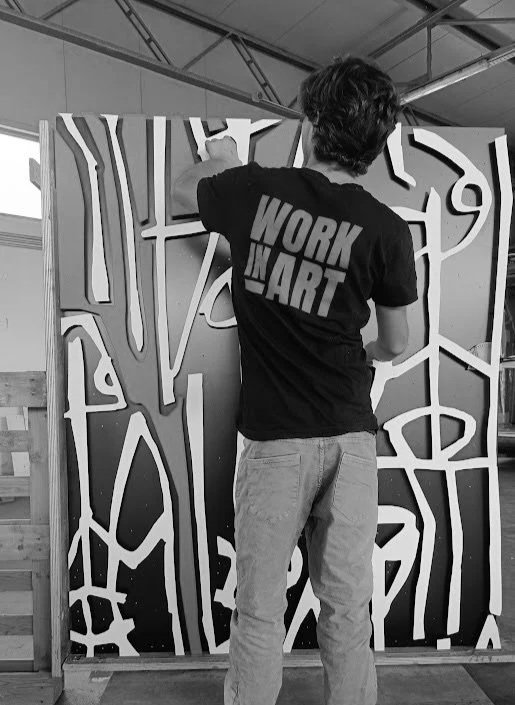 Una persona che dipinge una parete con un disegno astratto bianco e nero in un locale di lavoro.