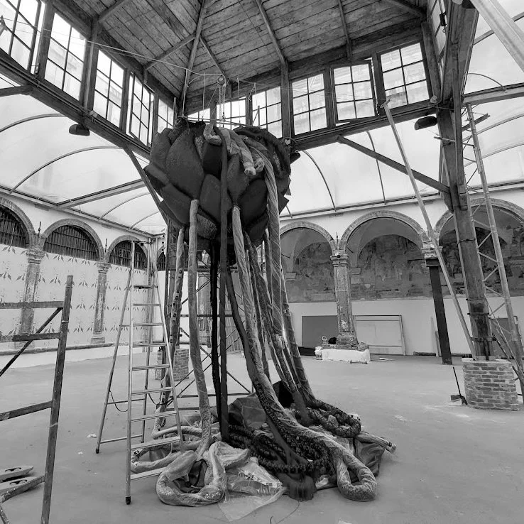 Installazione artistica di un gigantesco ragno in un ambiente di tipo industriale o artistico, con soffitto a volta in vetro e archi in pietra.