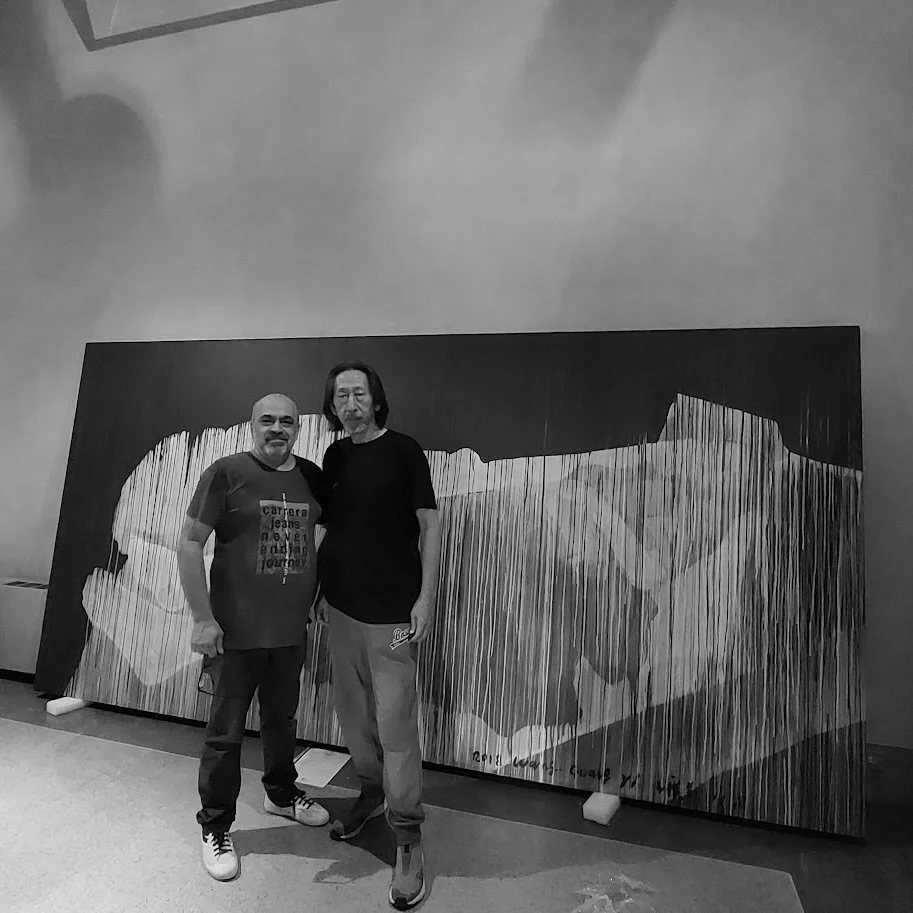 Due persone davanti a un grande dipinto astratto in bianco e nero, che rappresenta figure umane stilizzate