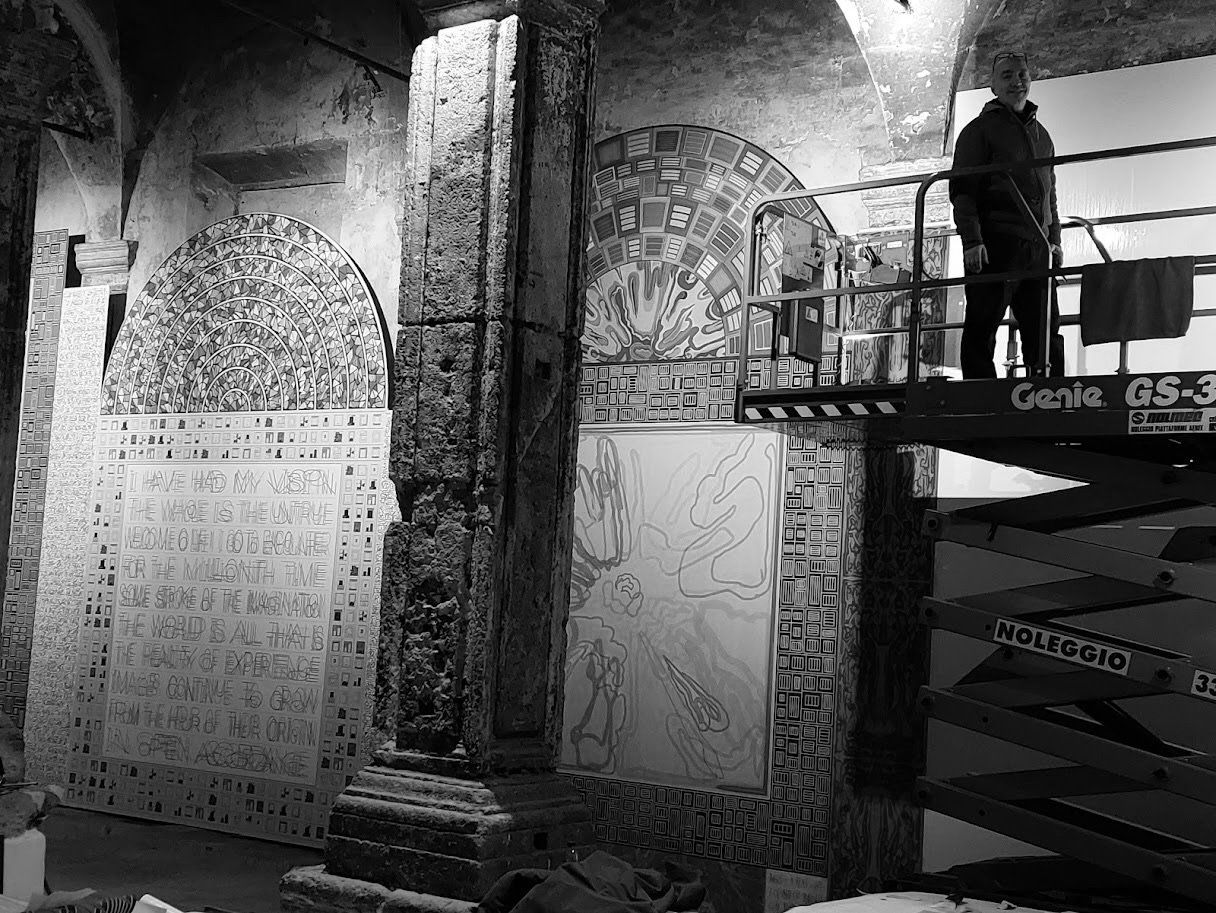 Interno di un luogo con pareti decorate con murales e scritte. C'è una persona su una piattaforma elevatrice.