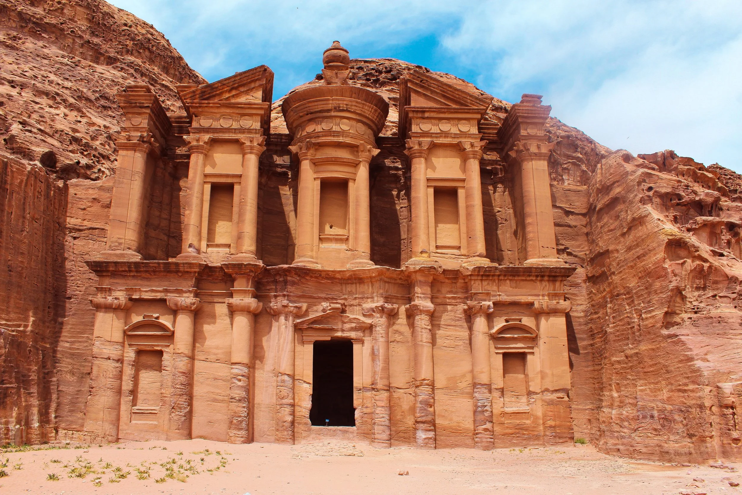 The historic Al-Khazneh (The Treasury) carved into the pink sandstone cliffs of Petra, Jordan, under a blue sky.