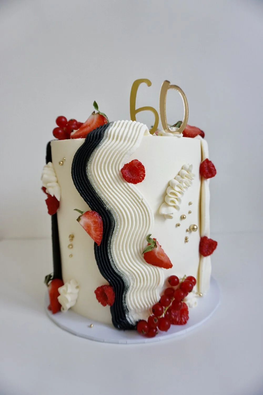 White birthday cake decorated with fresh strawberries, raspberries, red currants, and gold and black accents, with a gold "50" cake topper.