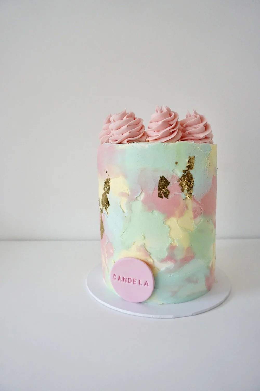 A pastel-colored marbled cake with pink frosting flowers on top and a pink circular topper with the name "Candela" on it.