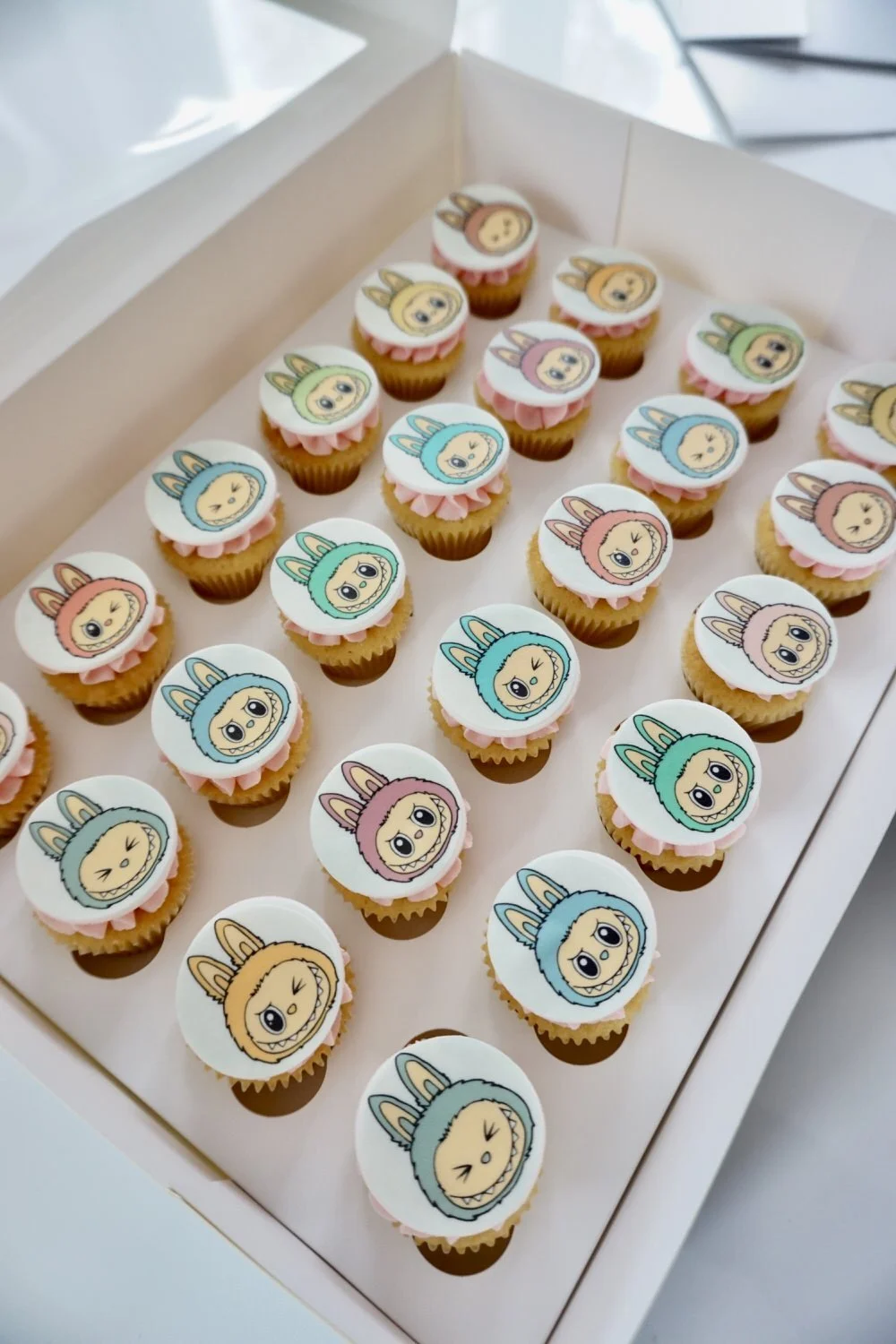 A tray of cupcakes decorated with edible images of cartoon characters with bunny ears in various colors.