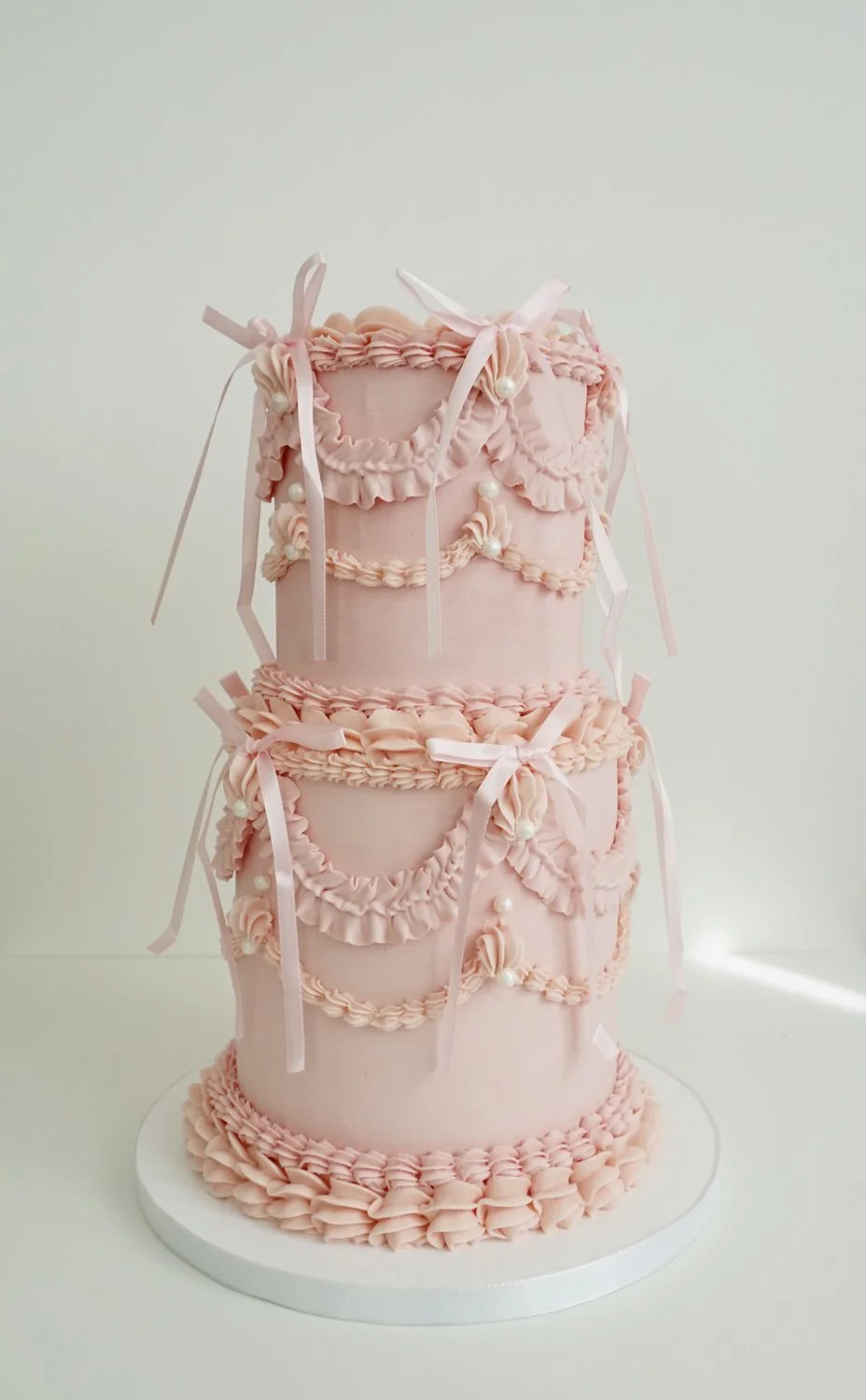 Three-tier pink wedding cake decorated with ruffles, bows, and pearl accents.