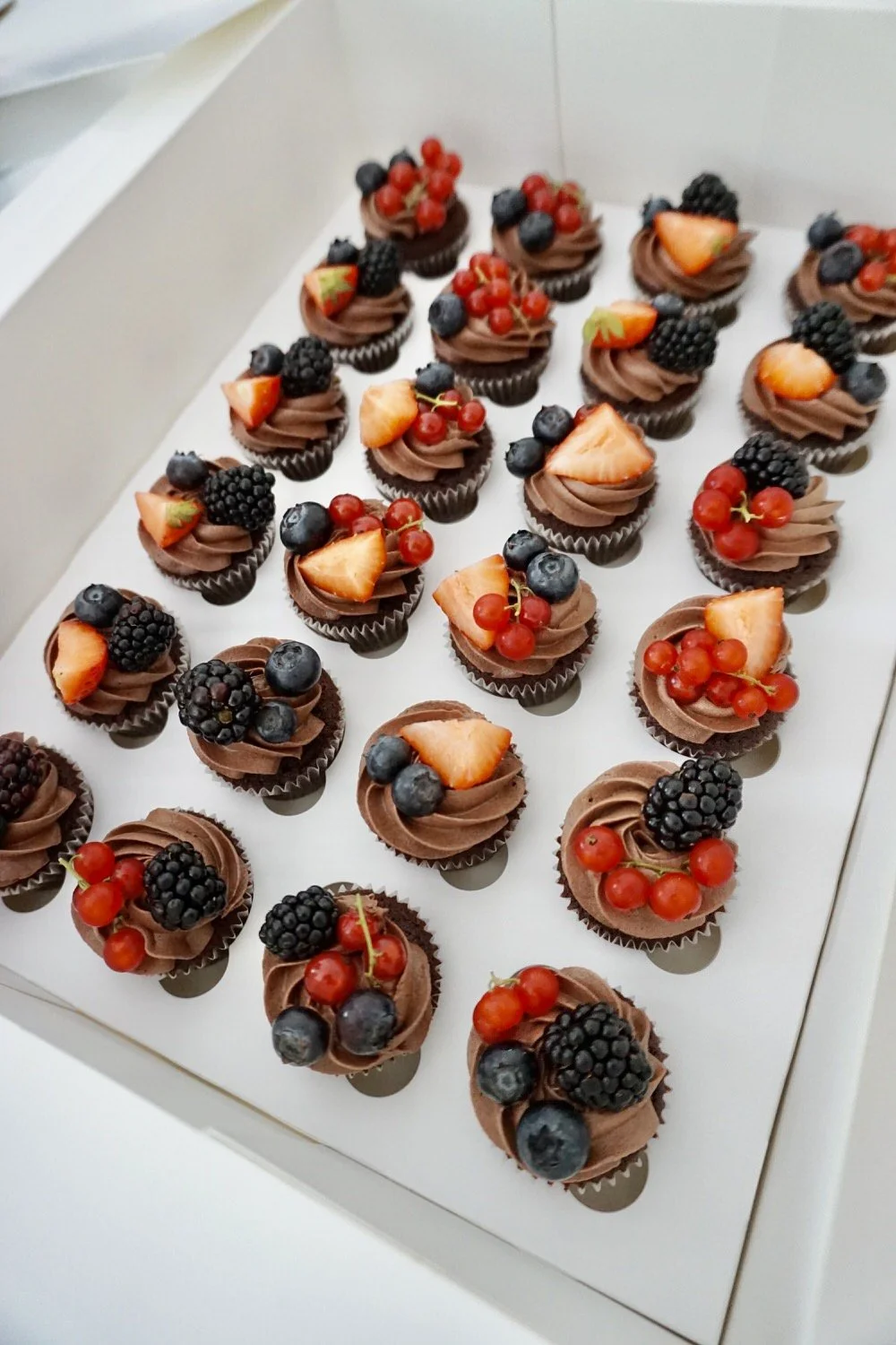 Chocolate cupcakes topped with mixed berries including blueberries, blackberries, and red currants, some with sliced strawberries.