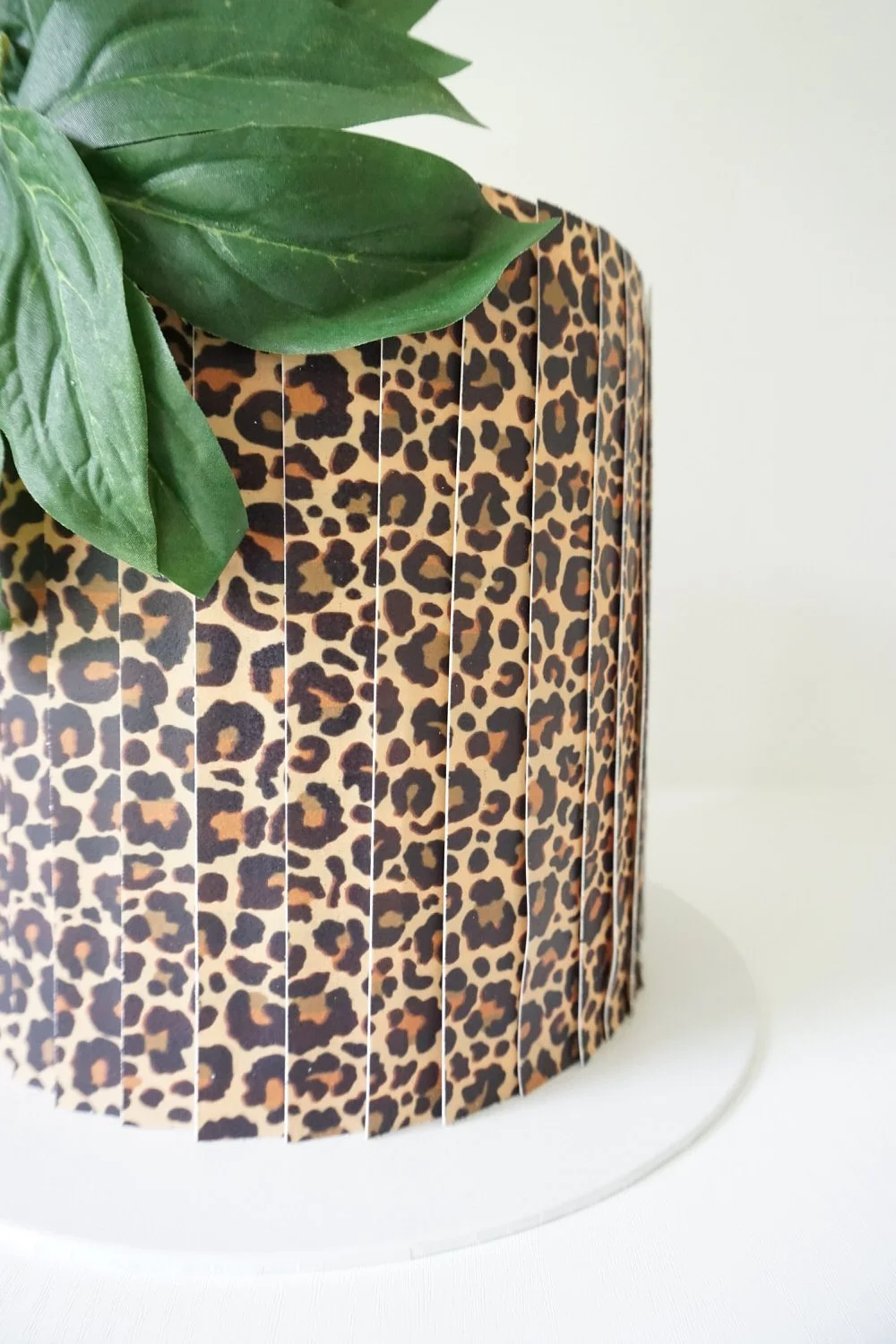 Close-up of a round cake with a leopard print pattern, decorated with green leaves on top.