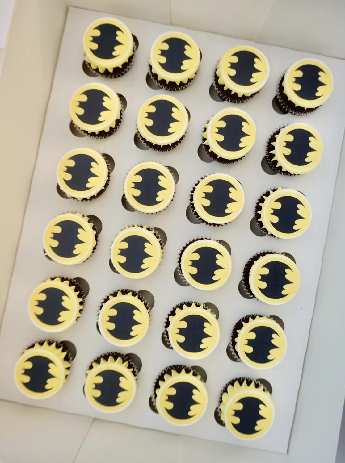 A white tray holding 20 cupcakes decorated with the Batman logo in yellow and black.