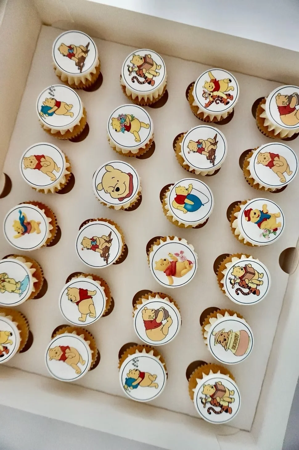Collection of cupcakes decorated with edible toppers featuring Winnie the Pooh characters, each with different poses and expressions.