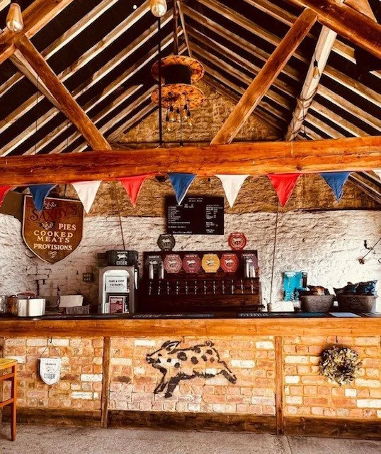 Interior of a rustic café or bar with exposed brick wall, wooden beams, and a counter decorated with a leopard graphic and festive bunting in red, white, and blue.