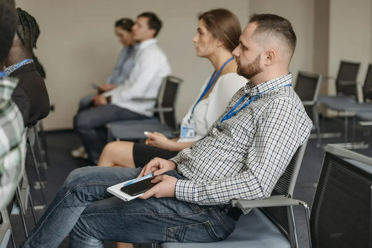 Groupe de personnes assises en réunion, attentives et prenant des notes, dans une salle de réunion moderne.