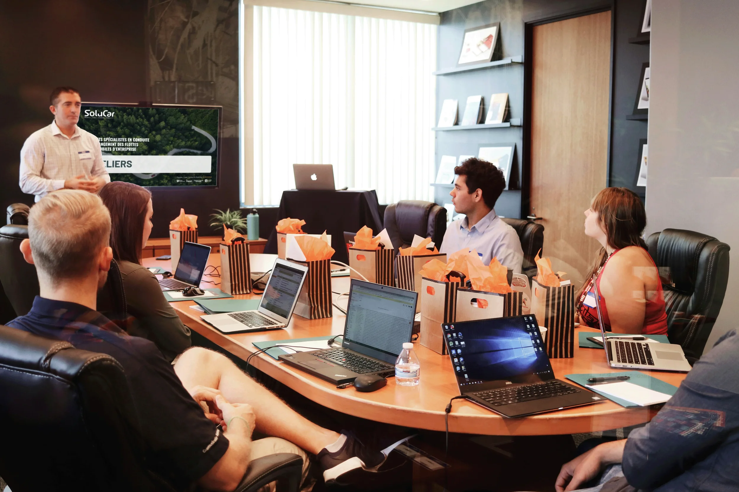 Une réunion dans une salle de conférence avec plusieurs personnes assises autour d'une grande table, un homme fait une présentation.