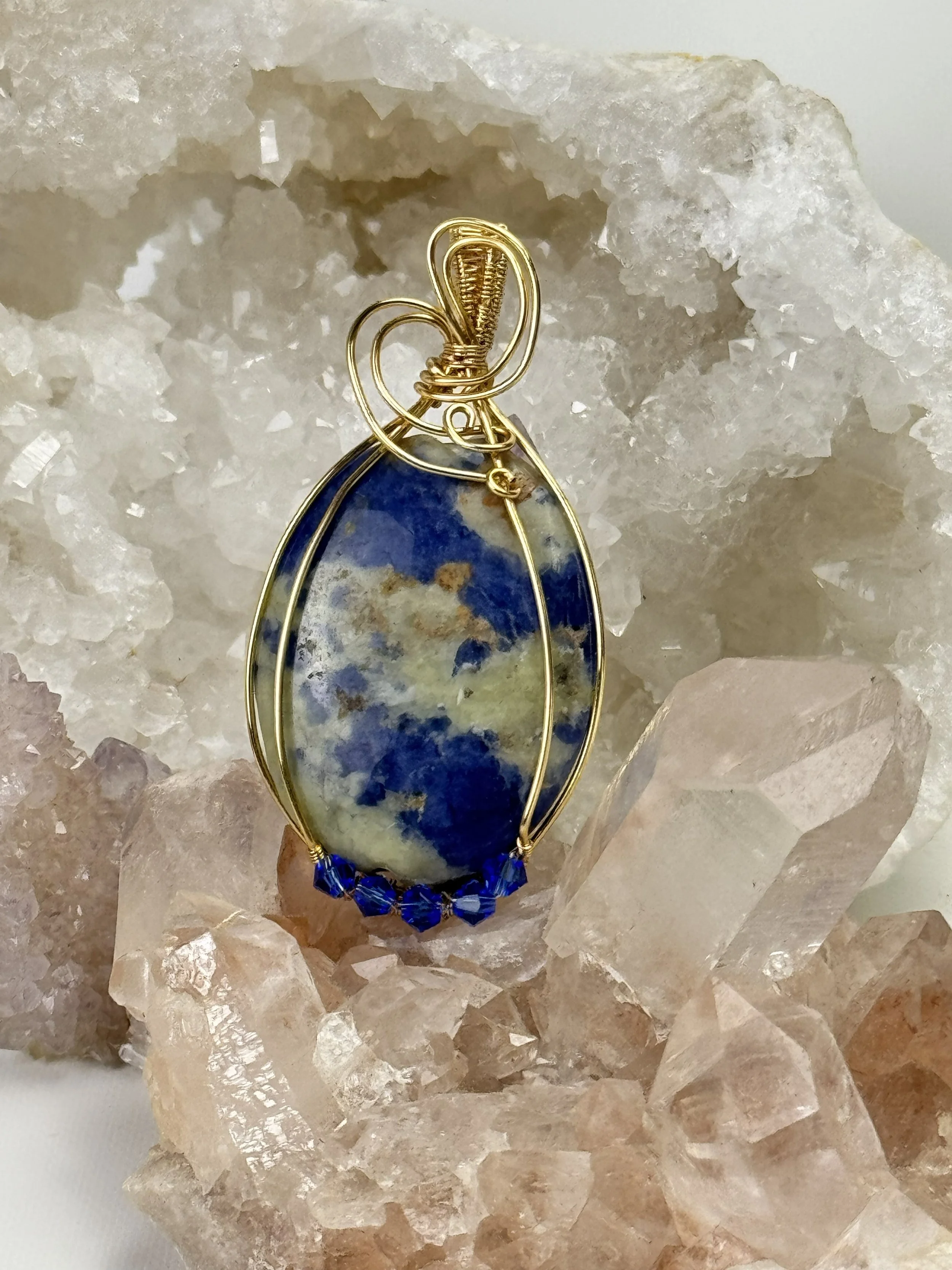 Hand-wrapped in warm gold-filled non tarnish wire, this striking pendant features a natural sodalite cabochon, accented by deep blue crystal beads along the base.  Each wrap is crafted by hand, ensuring no two pieces are ever exactly alike.