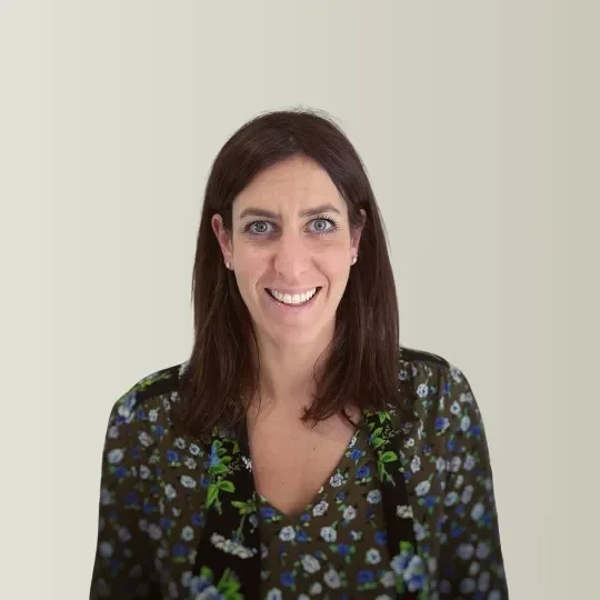 A woman with brown hair and blue eyes smiling at the camera against a neutral background.
