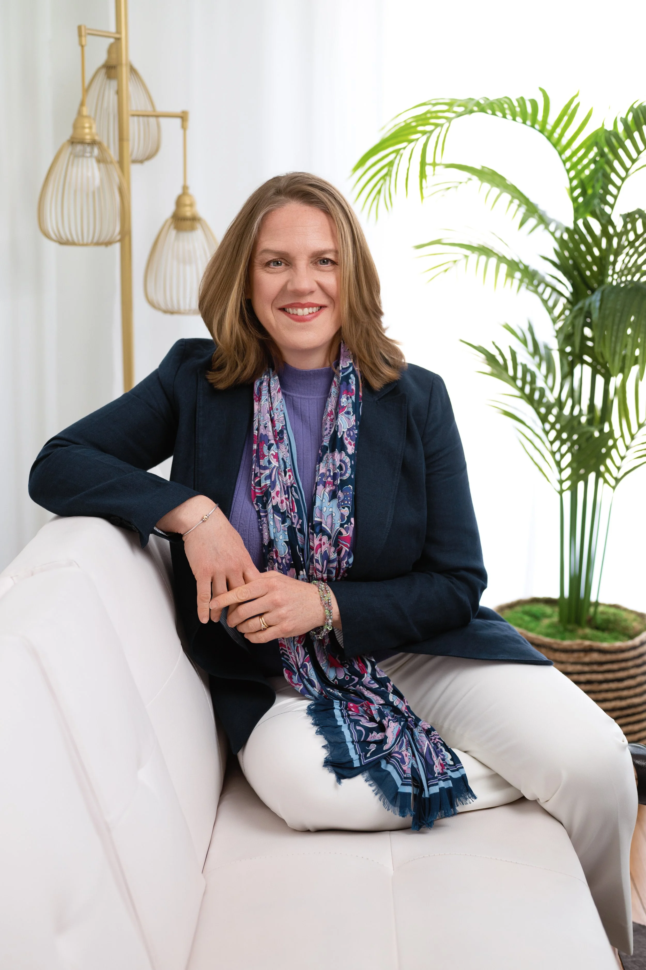 a women seated on a white sofa facing the camera and smiling