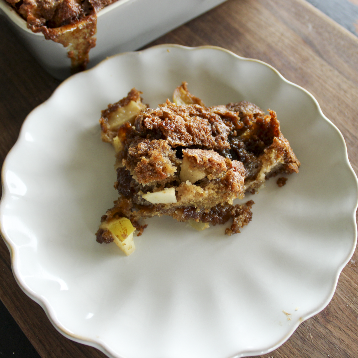 coffee cake with apples, sitting on a white scalloped plate on wooden cutting board