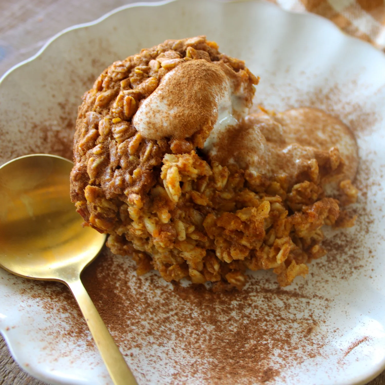 oats baked into a pumpkin custard, making an oatmeal bake, topped with greek yogurt and cinnamon, served on a white plate with a golden spoon