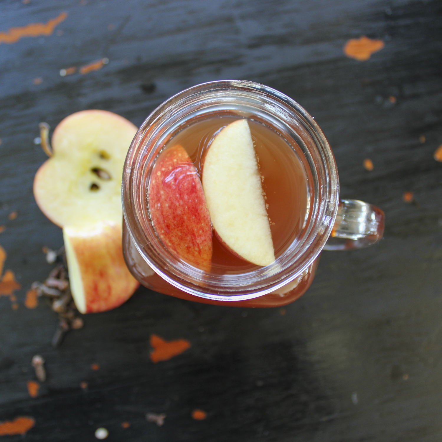 apple slices sitting in a glass cup full of apple cider, on a black table with a apple cut in half