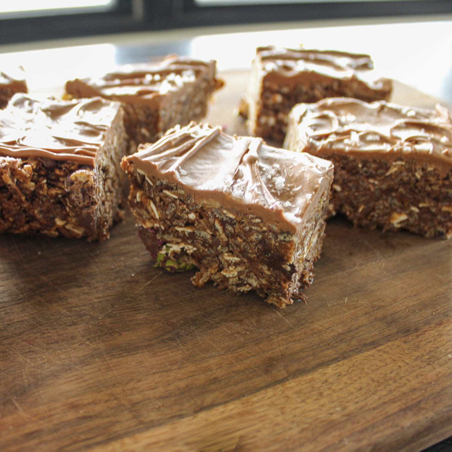 scotcharoos made with chocolate crispies, oatmeal, and chocolate candies, covered in chocolate topped with sea salt, sitting on a wooden board