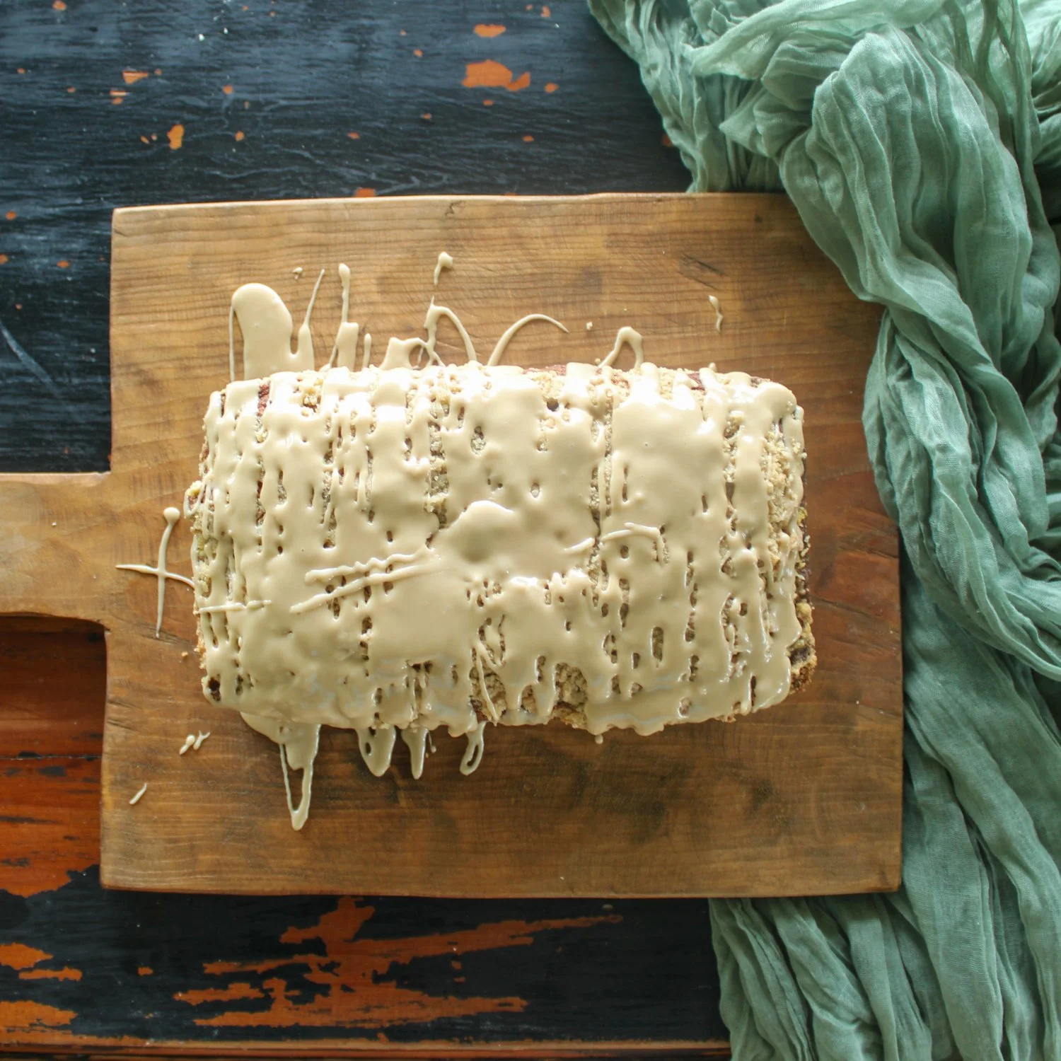 a coffee cake, made with pumpkin, drizzled with a glaze, sitting on a wood cutting board and a green towel beside it.