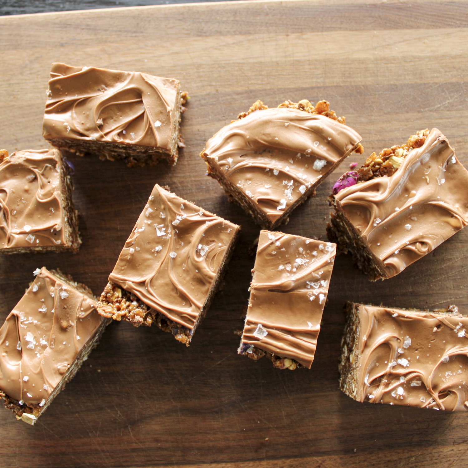 chocolate Rice Krispie treats covered in chocolate with sea salt on top, candy coated chocolates showing, sitting on a wooden board