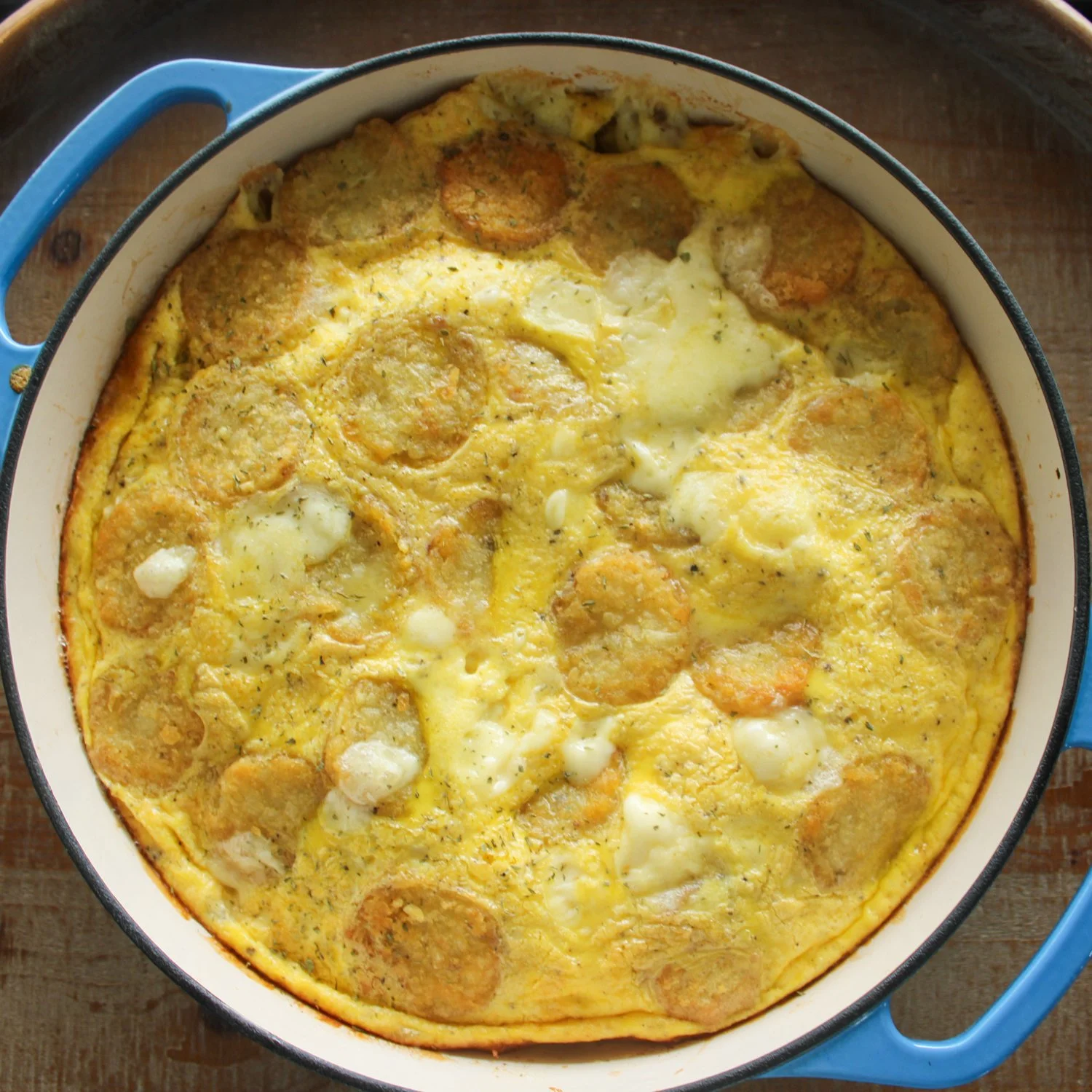 an egg bake in an enameled cast iron pan with blue handles, sitting on a wooden board.