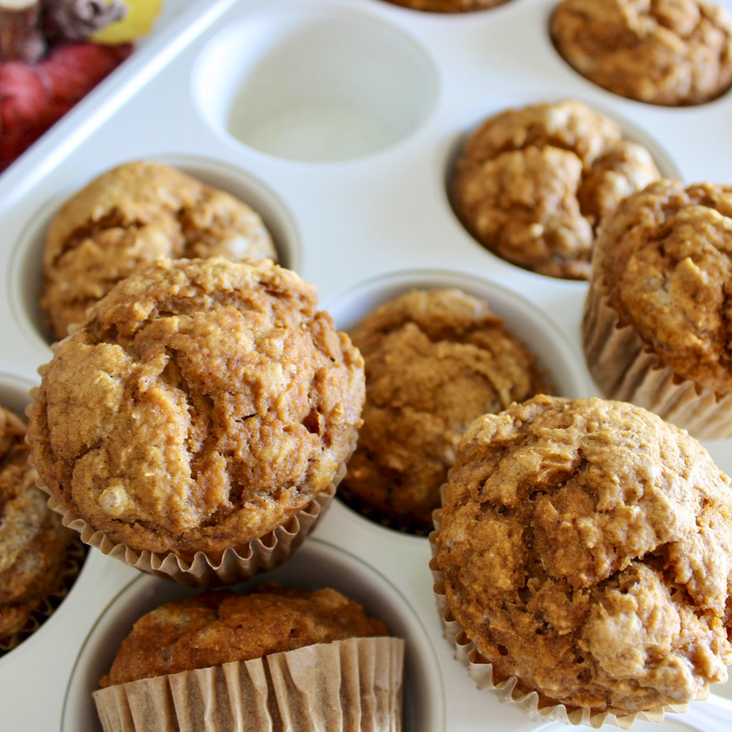 pumpkin muffins in parchment wrappers, sitting on a white muffin tin