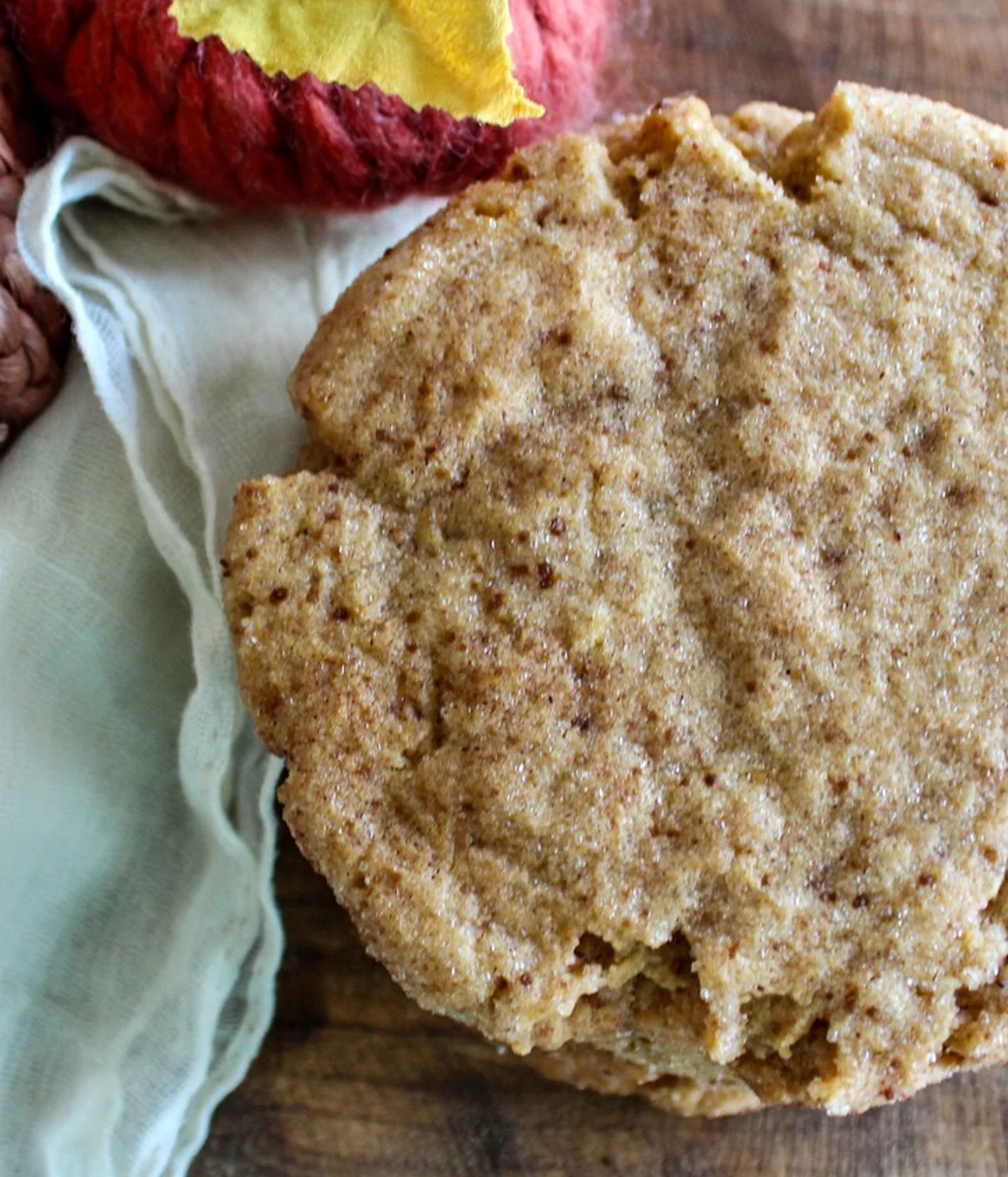 pumpkin snickerdoodle cookie rolled in coconut sugar, sitting on a cream cloth napkin with an orange pumpkin made of yarn