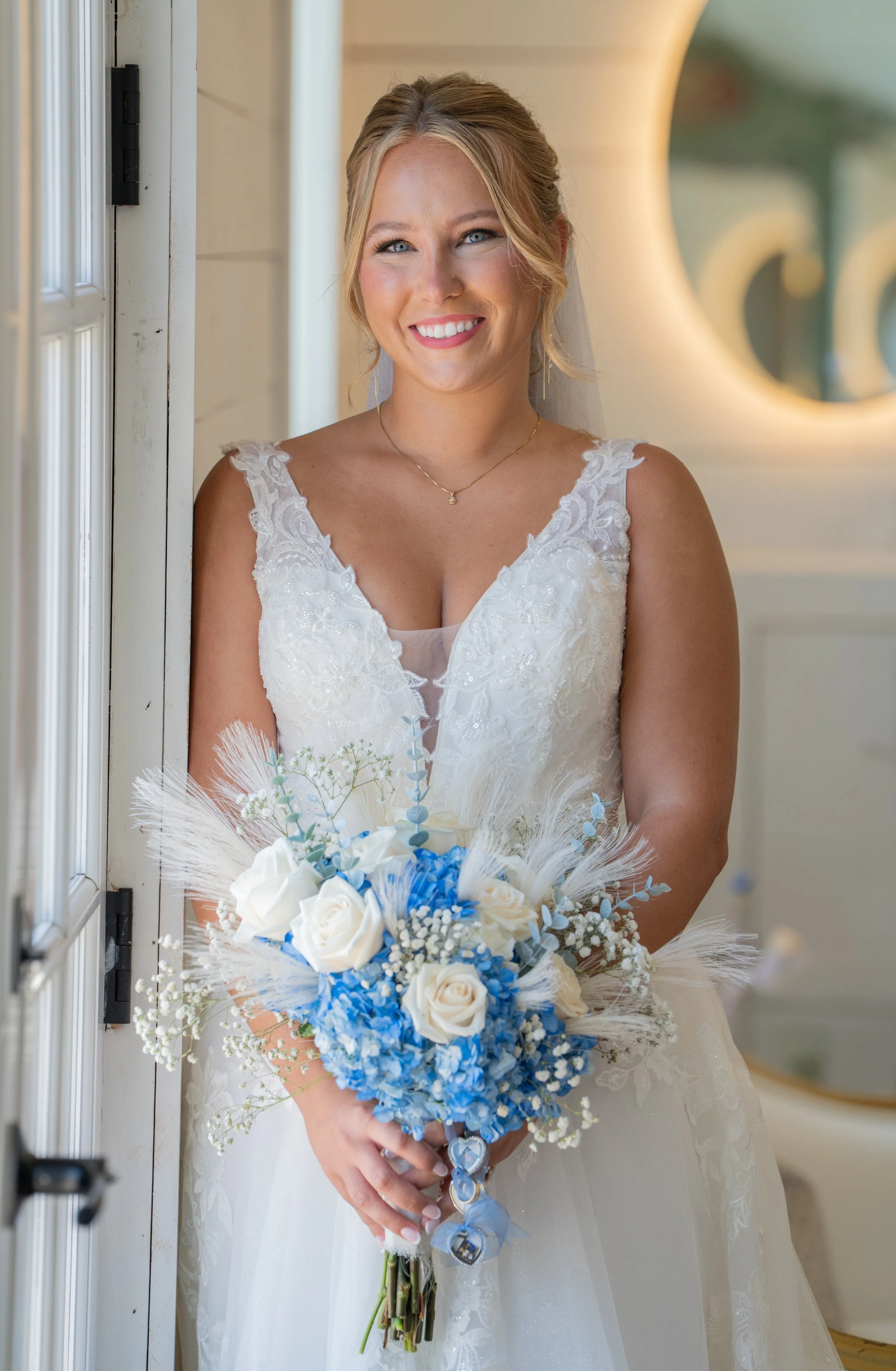 A smiling woman in a wedding dress holding a bouquet of white and blue flowers.