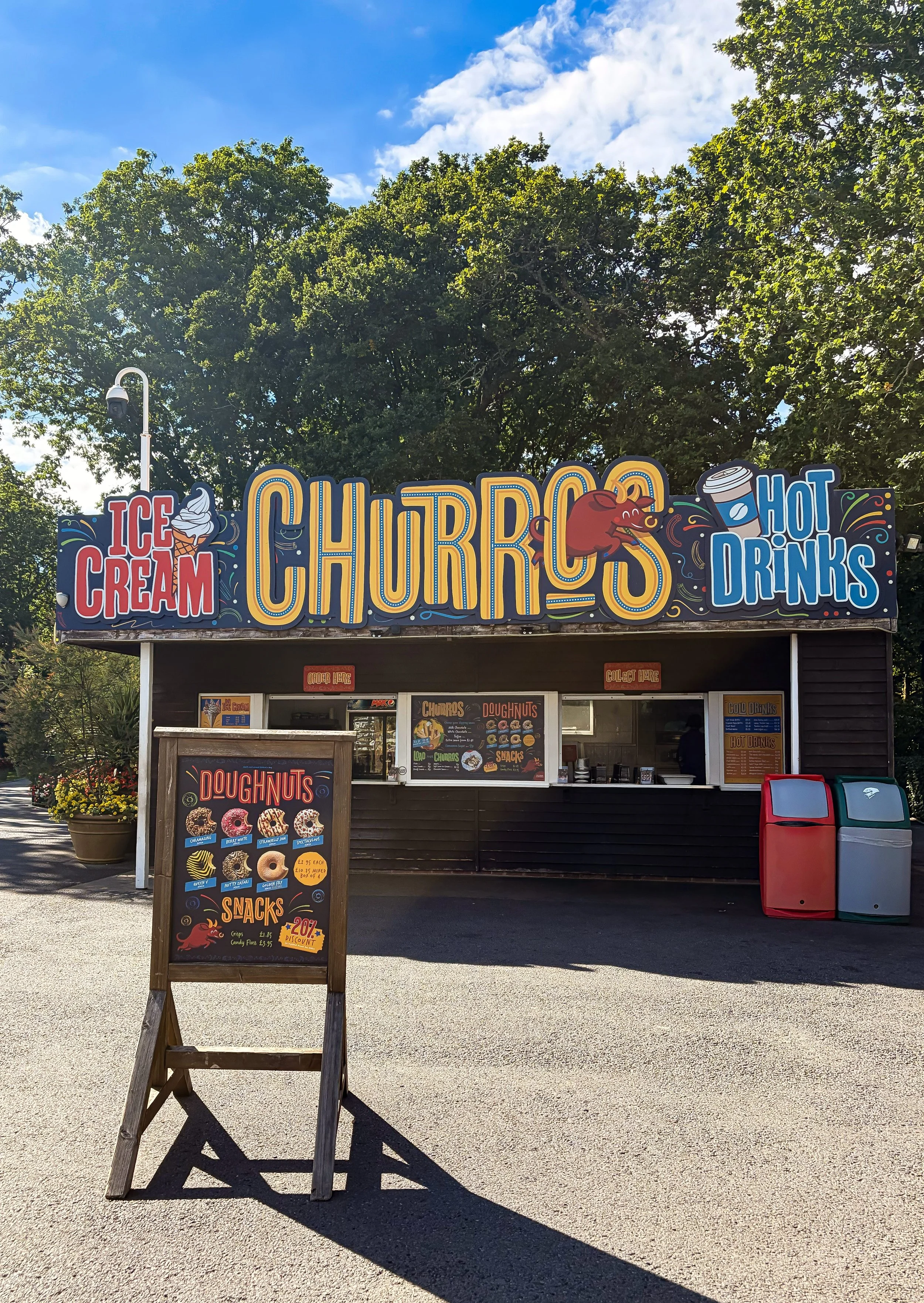Food kiosk with big bold yellow text on top reading Churros, Ice Cream and Hot Drinks with a navy background and red bull cartoon
