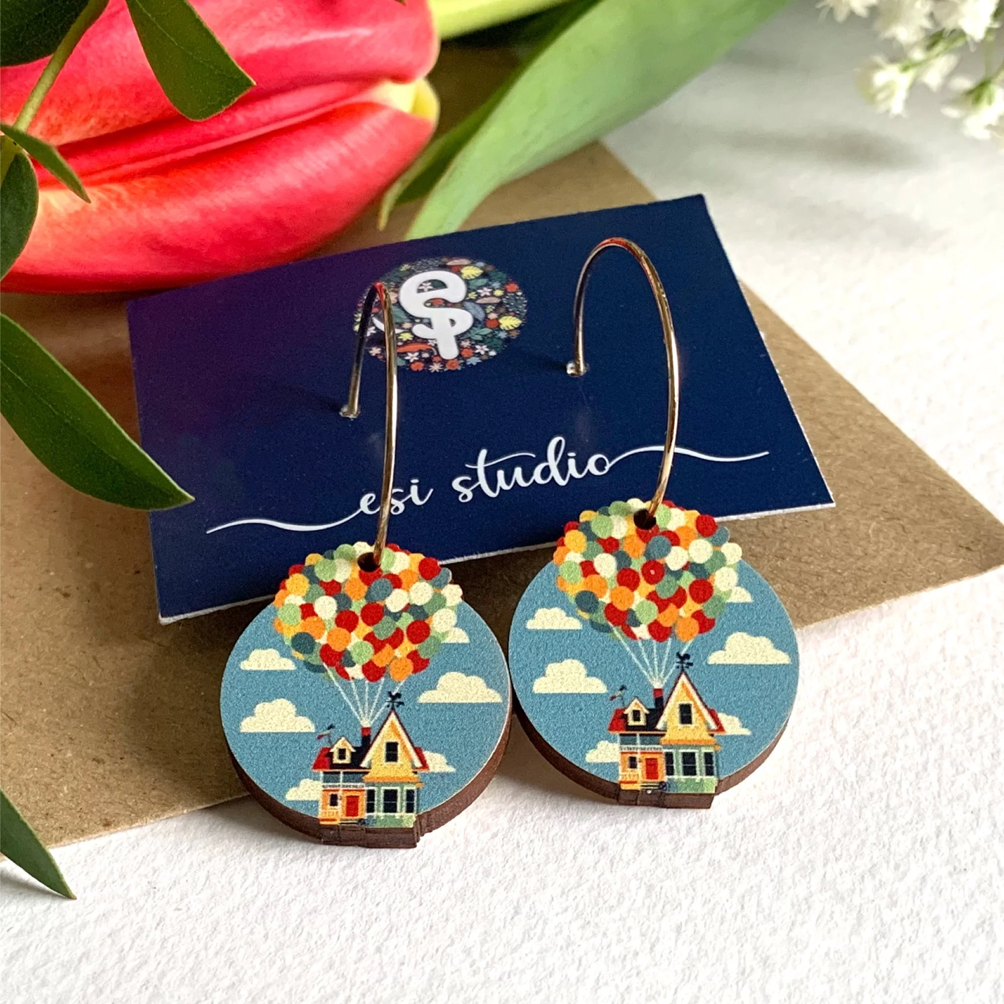 House suspended by multiple balloons in the sky cut to shape earrings on golden hoops.