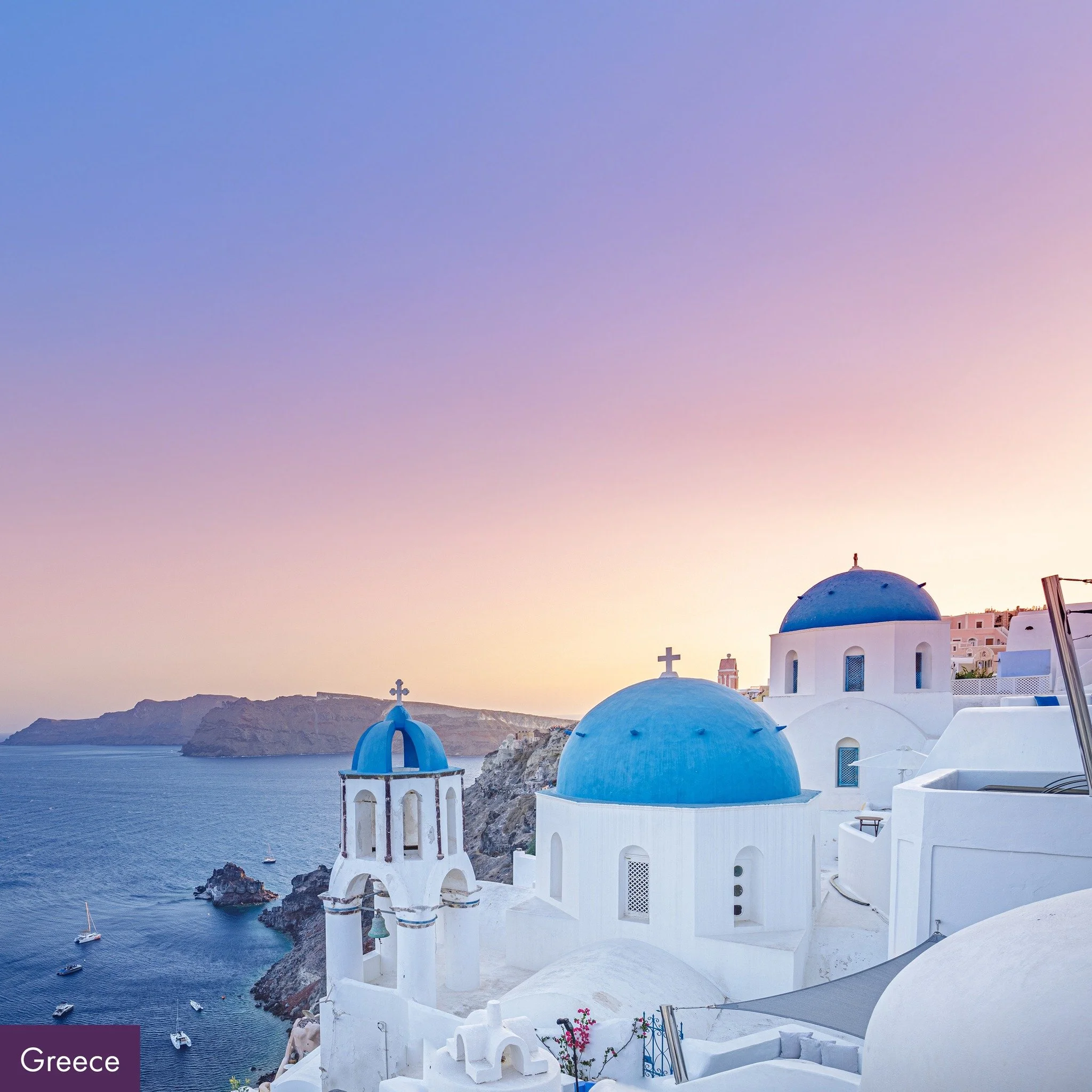 White buildings with blue domes on a cliff overlooking the Aegean Sea in Santorini, Greece, at sunset.