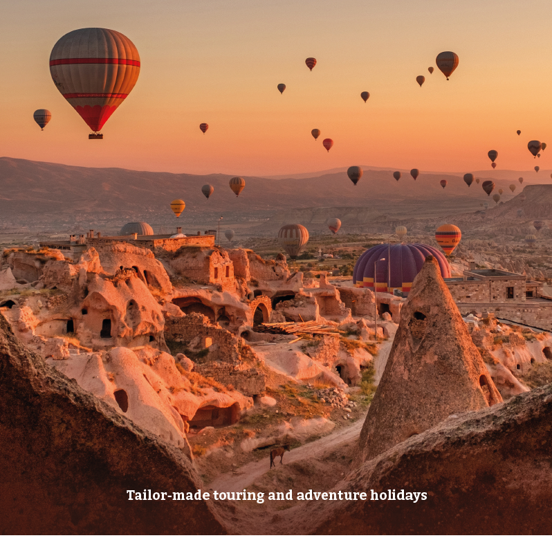Hot air balloons floating over ancient rock formations and cave dwellings during sunset in Cappadocia, Turkey.
