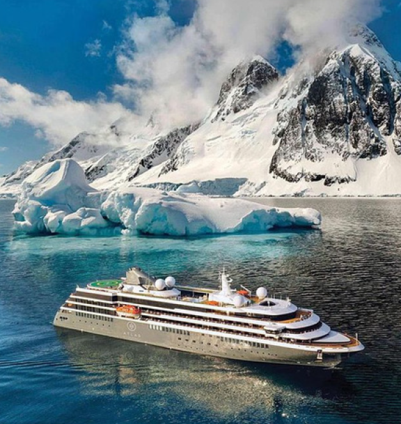A cruise ship sailing near icebergs and snow-covered mountains in a cold, polar region.