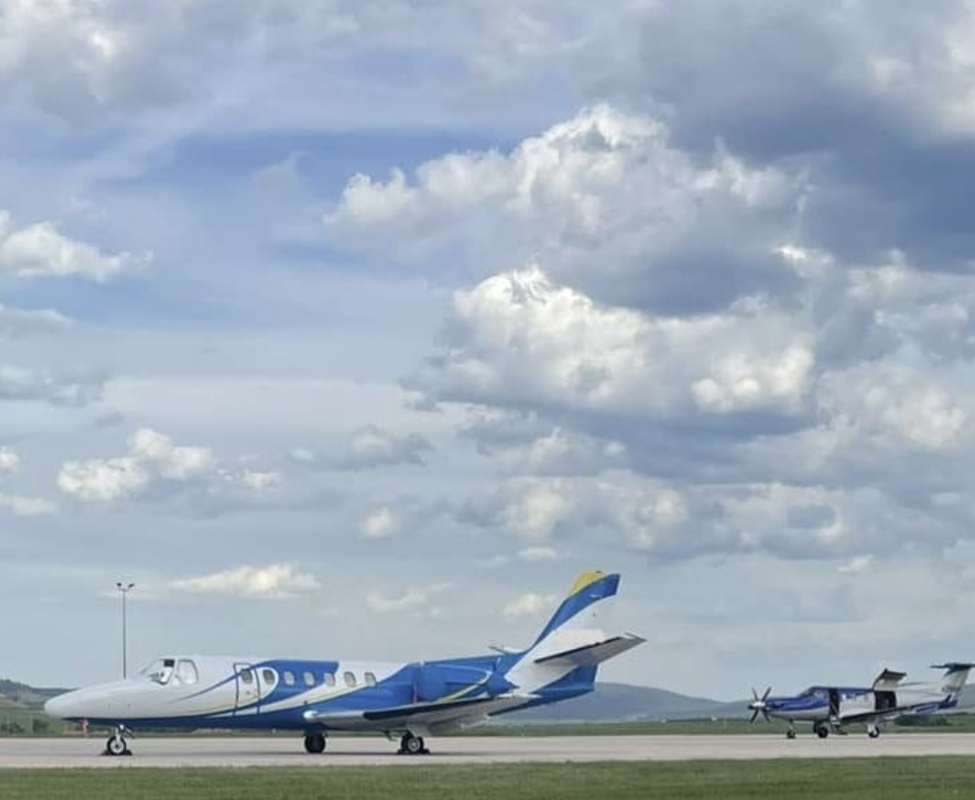 Two private jet airplanes parked on a runway with a cloudy sky overhead.