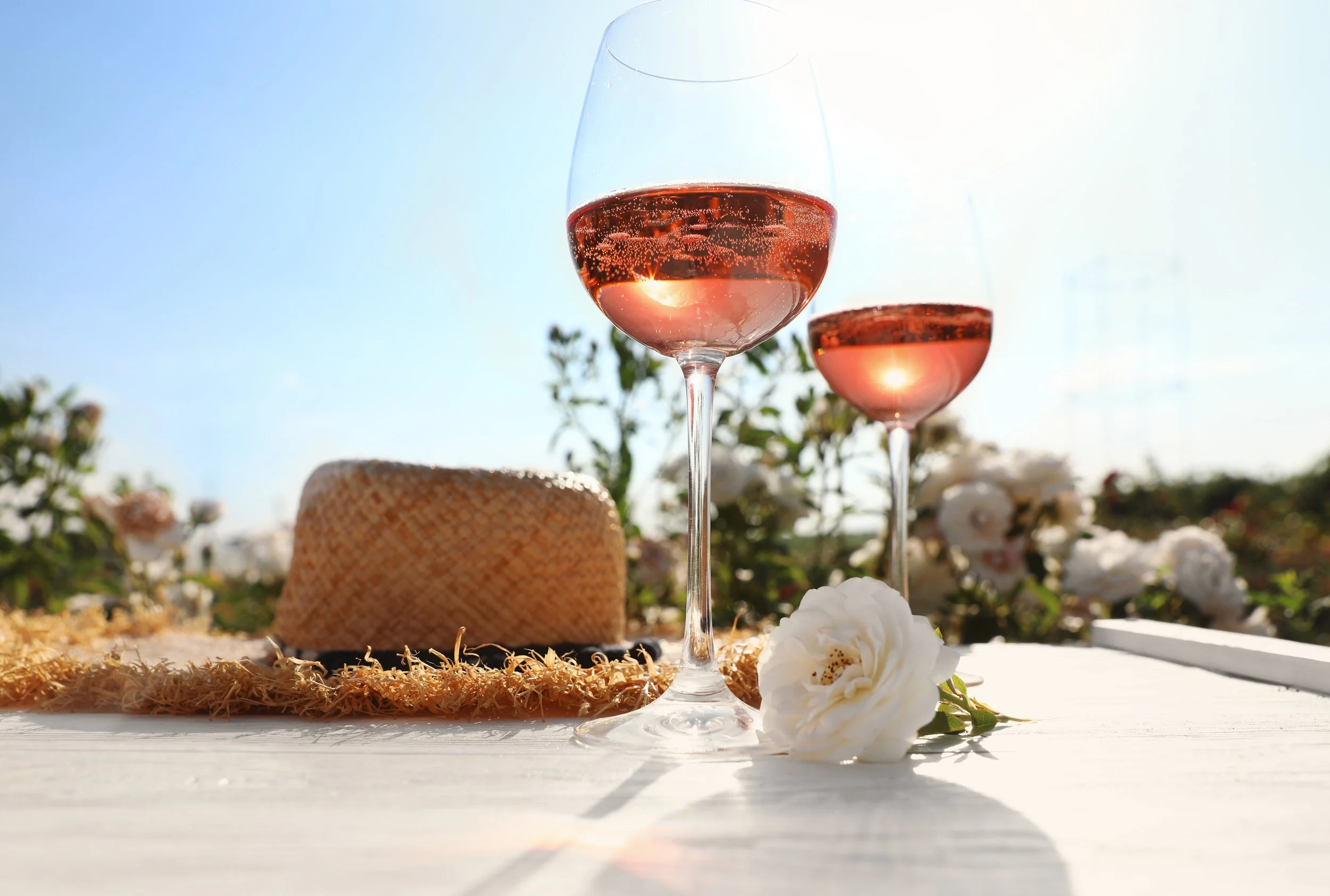 Two glasses of refreshing rose and a straw hat and rose on a picnic table