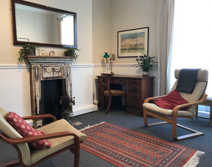 Cozy living room with vintage fireplace, mirror, desk, armchair with pillow, and a rug.
