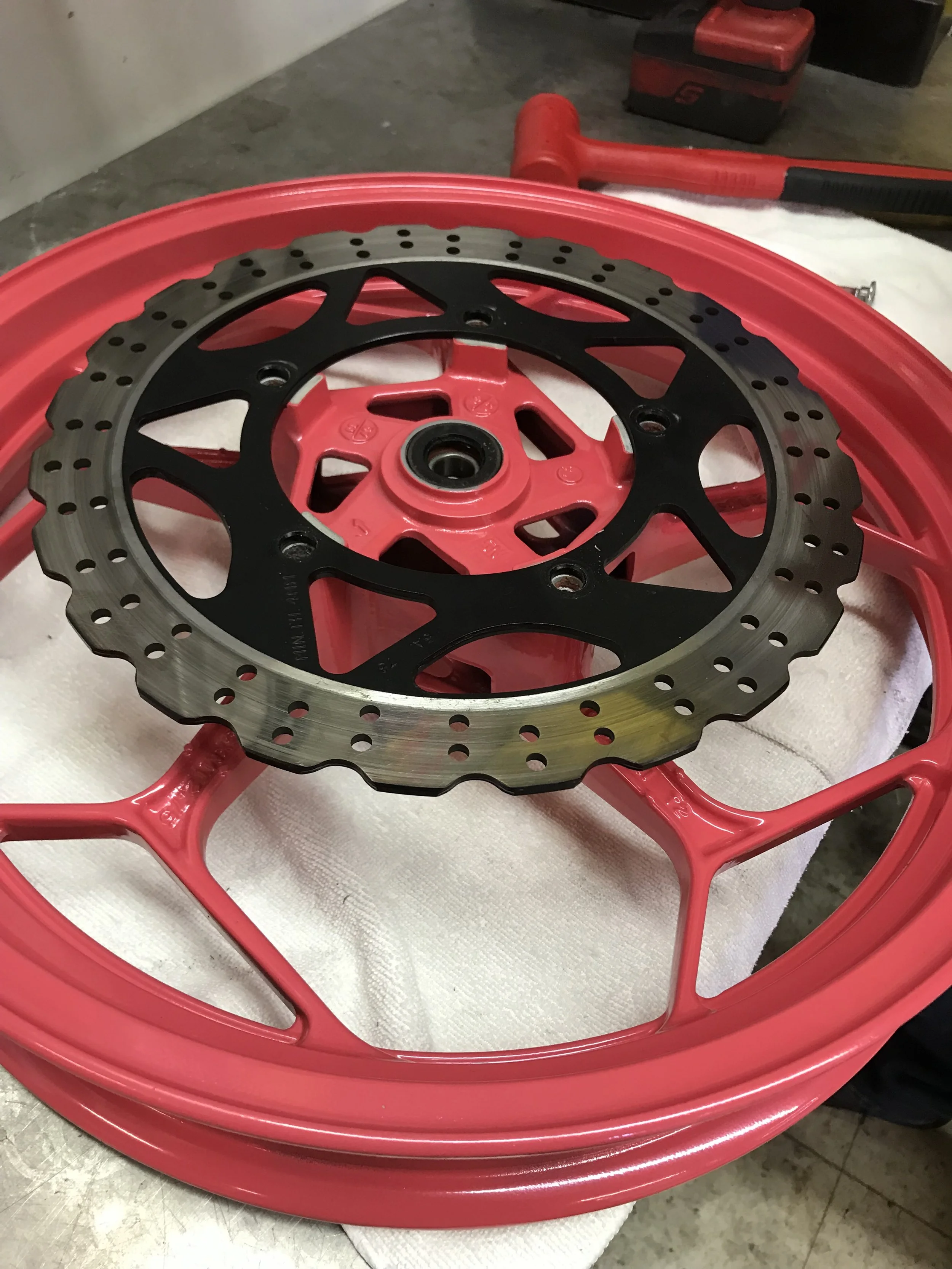 A red motorcycle wheel with a brake disc and caliper attached, resting on a white cloth on a work surface.