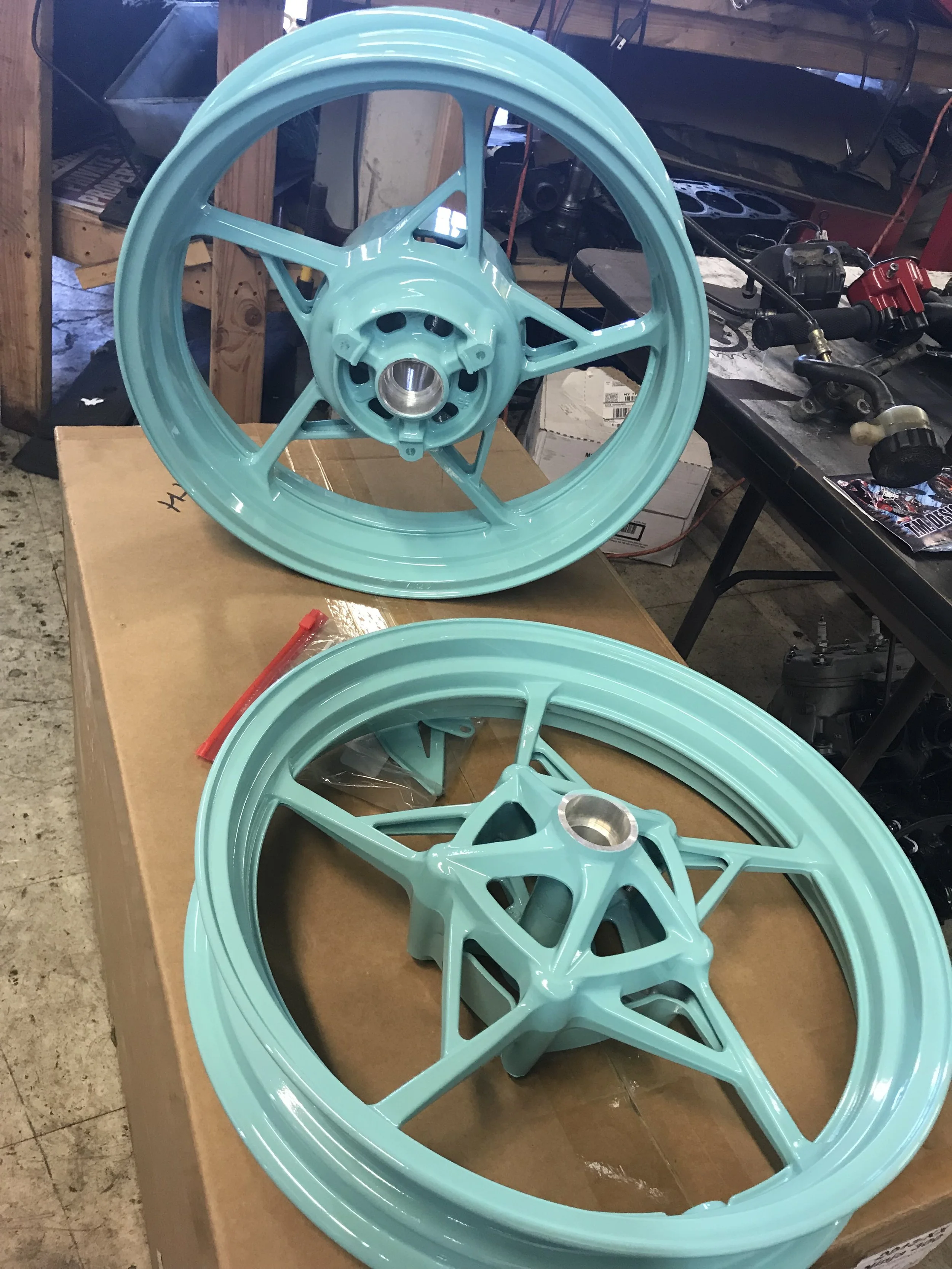 Two turquoise motorcycle wheels on a workbench in a garage.