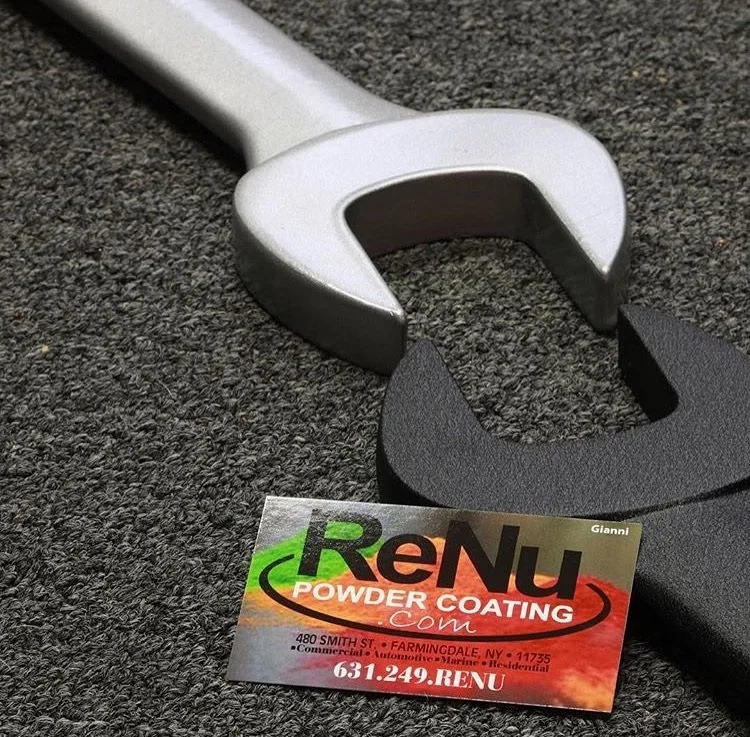 A silver wrench and a black plastic pry tool resting on a textured surface, with a business card for RenU Powder Coating beneath them.
