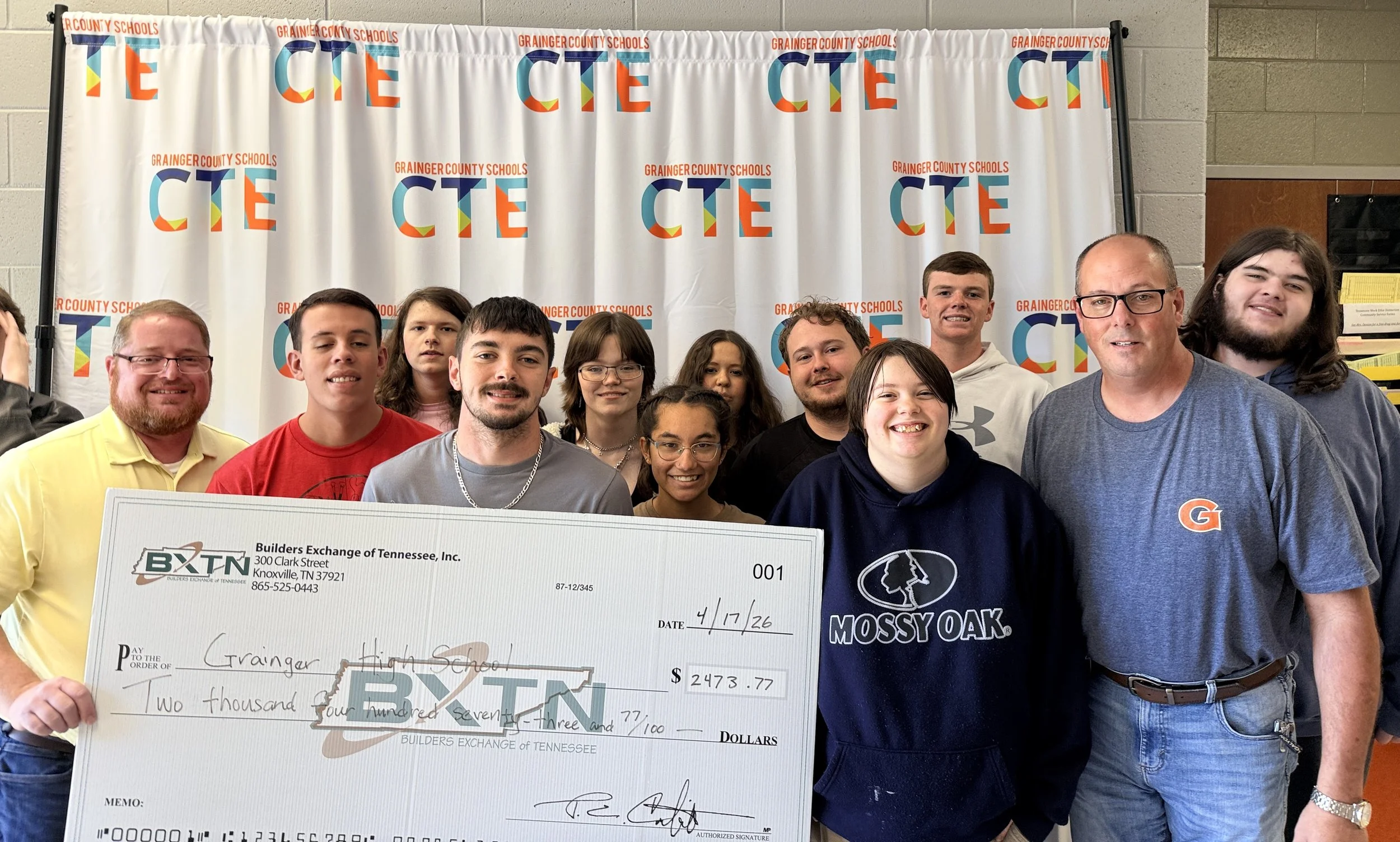 A group of students and adults holding a large check in front of a backdrop with the text 'Grainger County Schools' and 'CTE' in colorful letters.