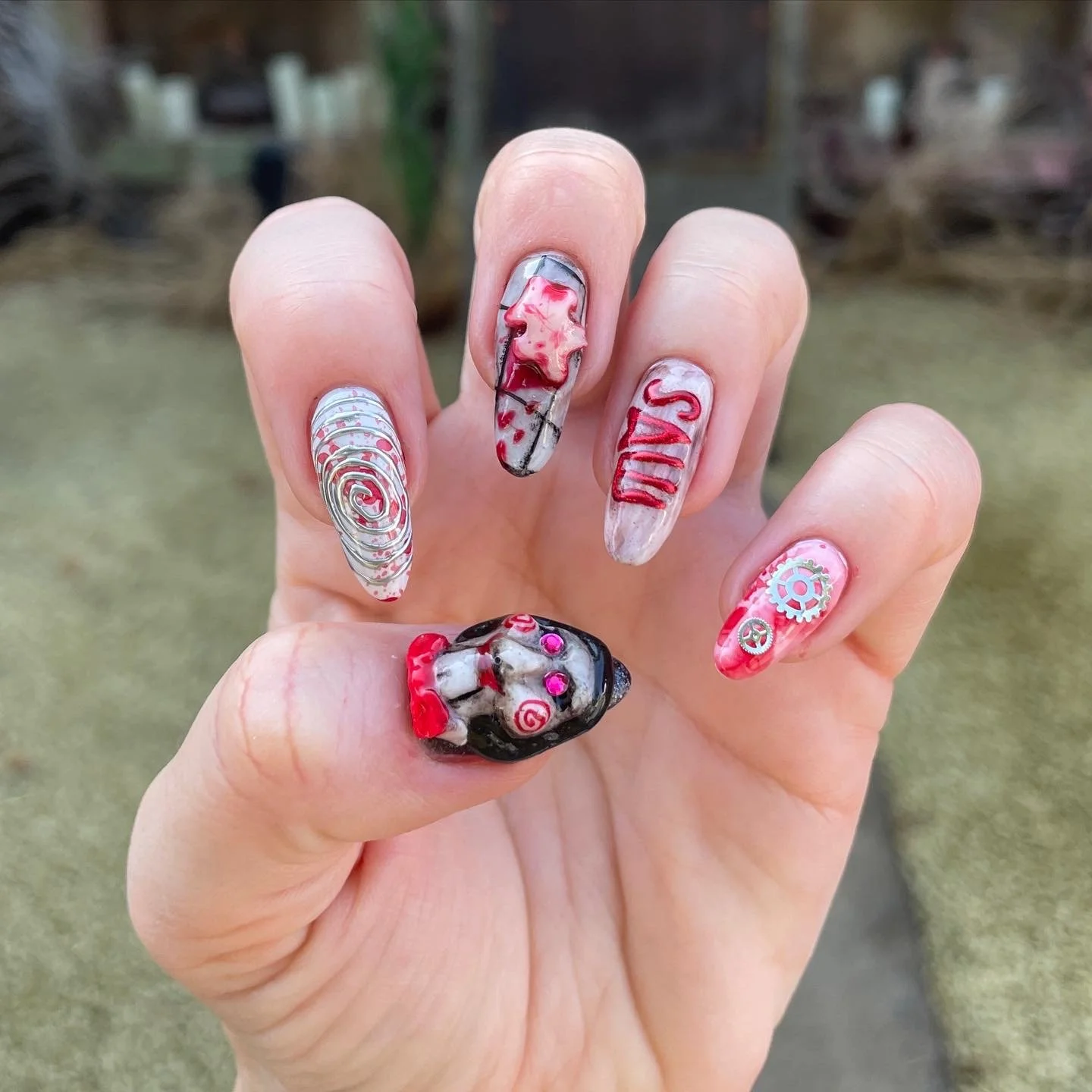 Close-up of a hand with decorated Halloween-themed nail art, including a skull, gears, and spooky designs in red, black, and white colors.