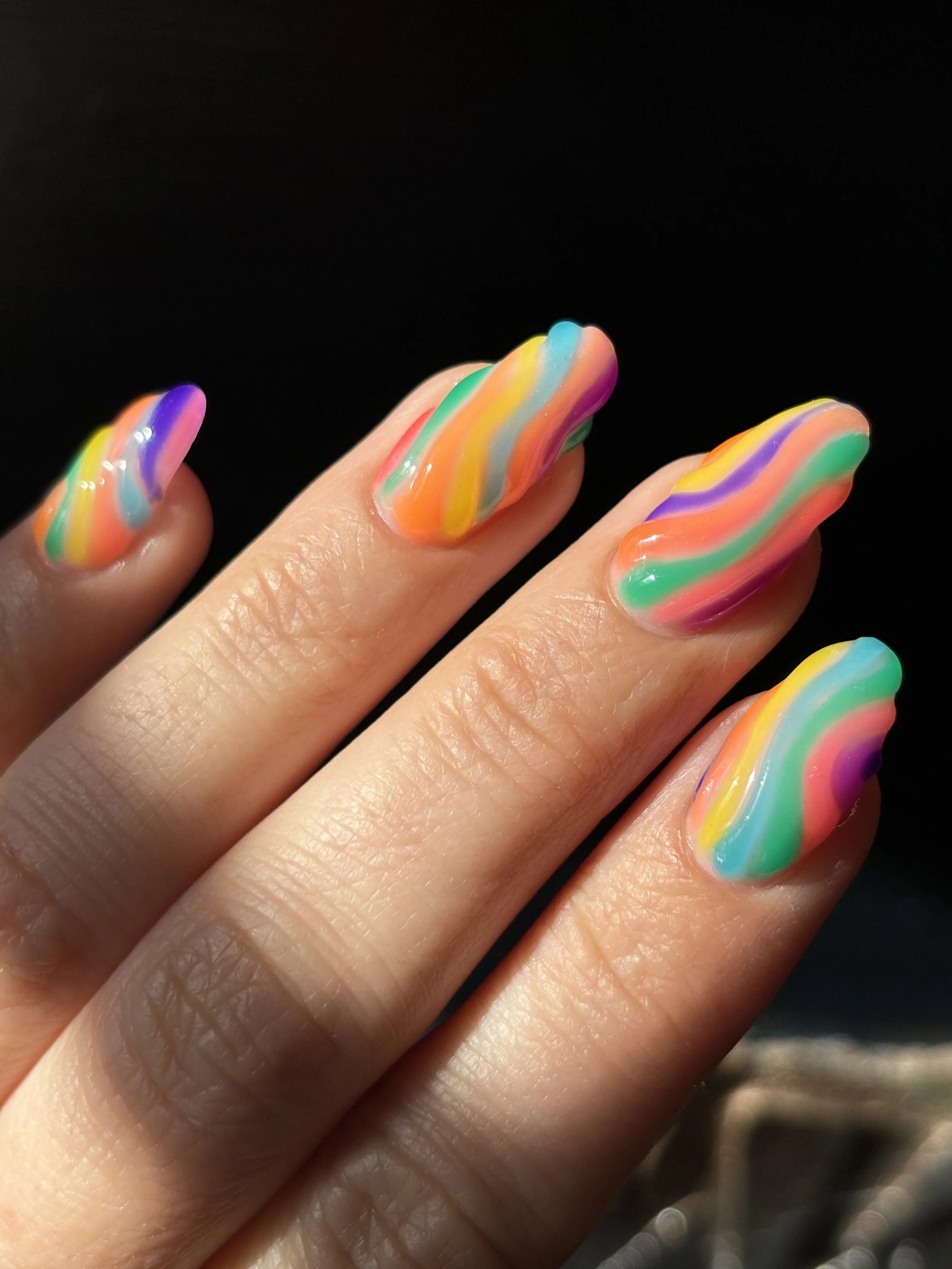 Close-up of four fingers with colorful rainbow swirl nail polish against a black background.